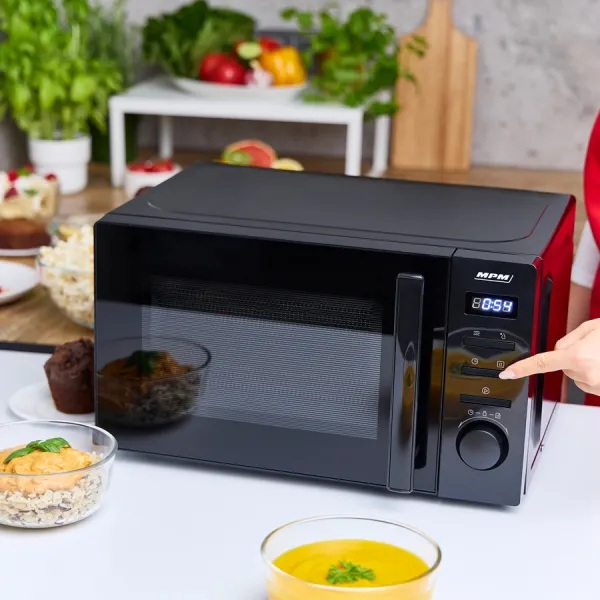 Czarna kuchenka mikrofalowa z jedzeniem. Ręka naciska przycisk na panelu sterowania.