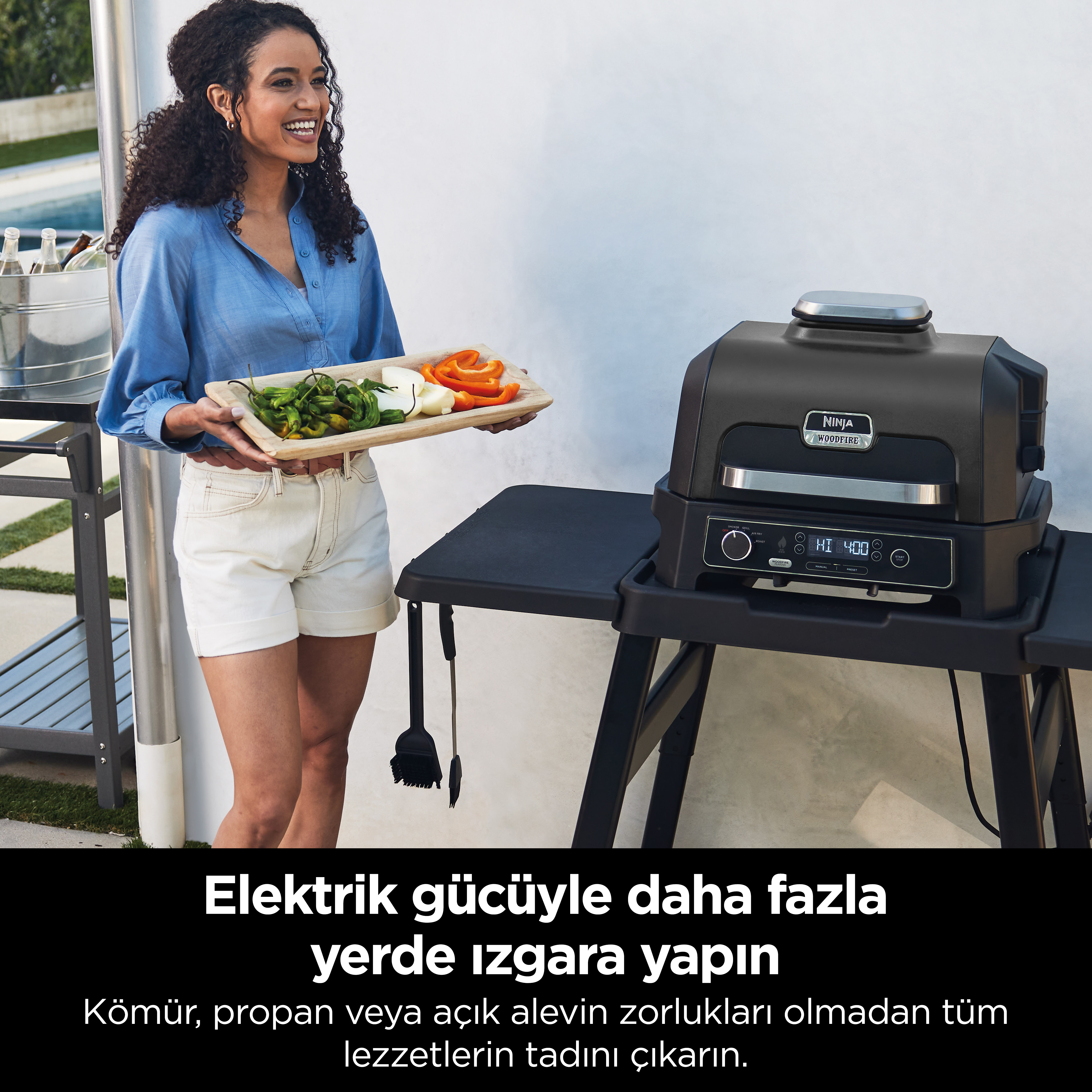 Bir kadın sebzelerle dolu bir tepsi tutuyor. Bir masada Ninja ızgarası. Metin yerleşimi: Elektrik gücüyle her yerde ızgara yapın.