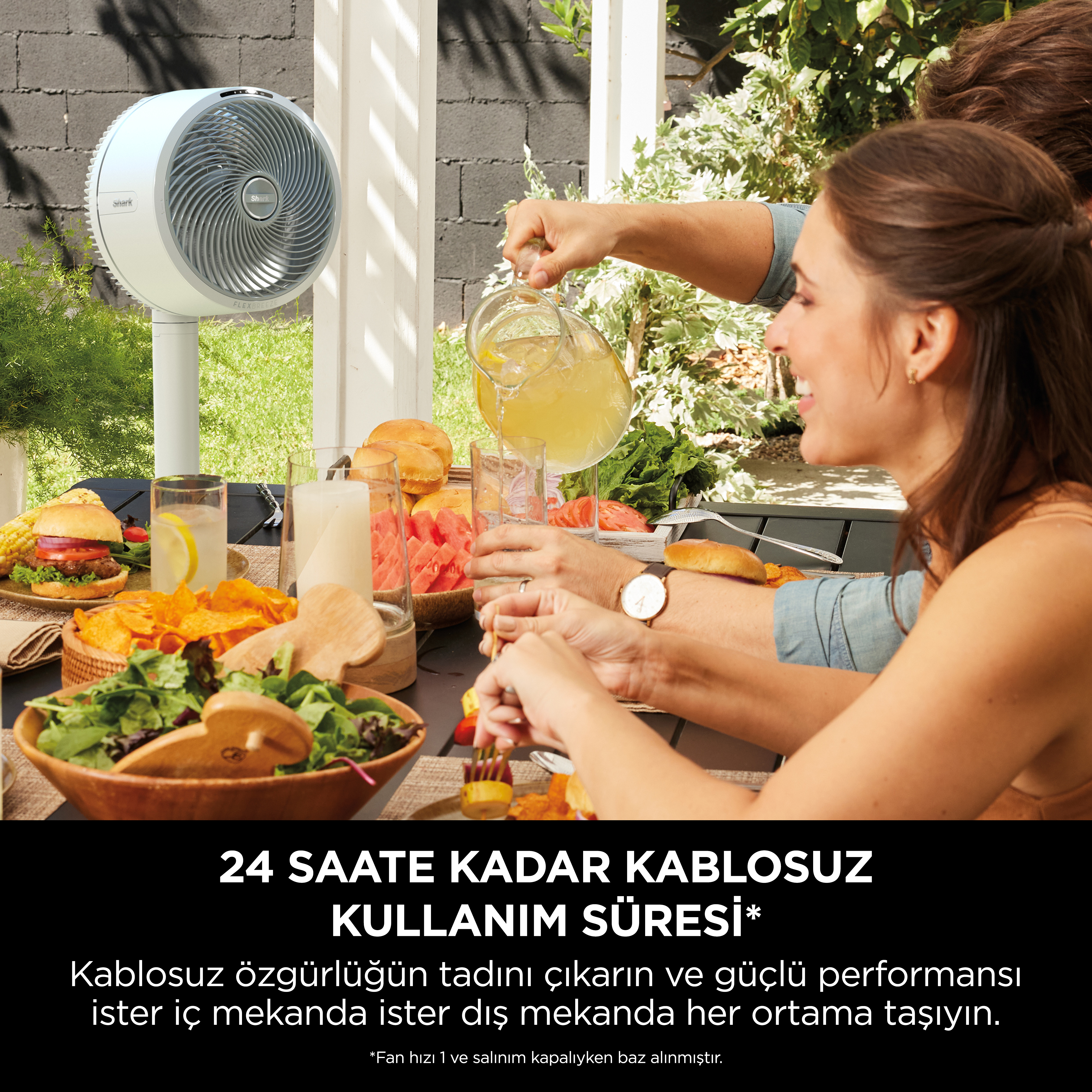 İnsanlar bir masada, beyaz bir vantilatör ve dışarıda yemek yiyor.