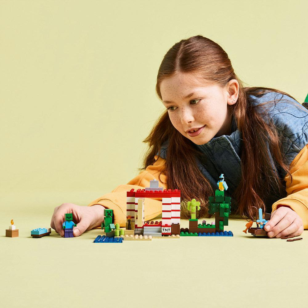 Mädchen spielt mit einem Lego Minecraft-Set. Sie interagiert mit den Figuren und der Hausstruktur.