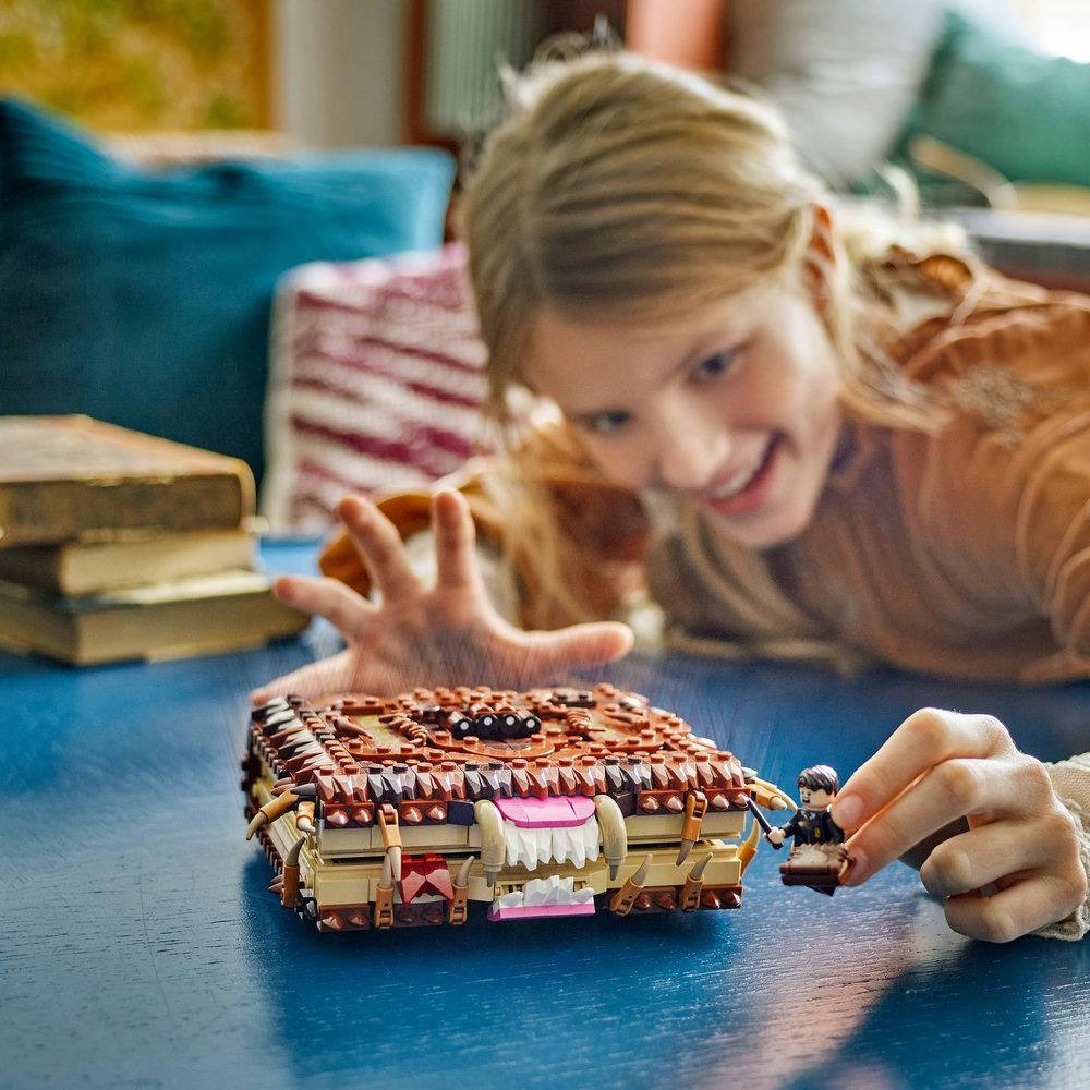 Ein Mädchen spielt mit einem Lego-Set eines Monsterbuches. Es gibt eine Lego-Figur und einen blauen Tisch.
