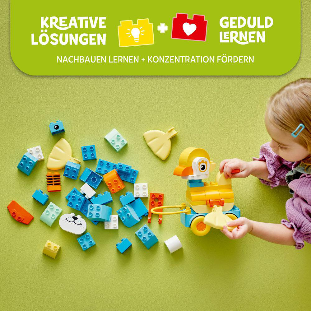 Mädchen spielt mit Lego Duplo-Blöcken. Blöcke sind verstreut, Entenspielzeug ist gebaut.