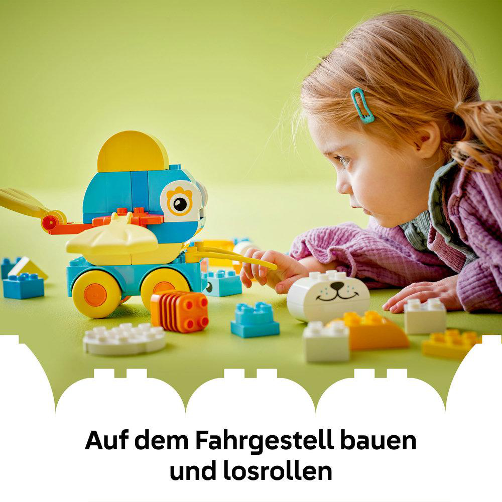 Mädchen betrachtet eine Lego Duplo Spielzeugente auf einer blauen Oberfläche. Blöcke sind in der Nähe.