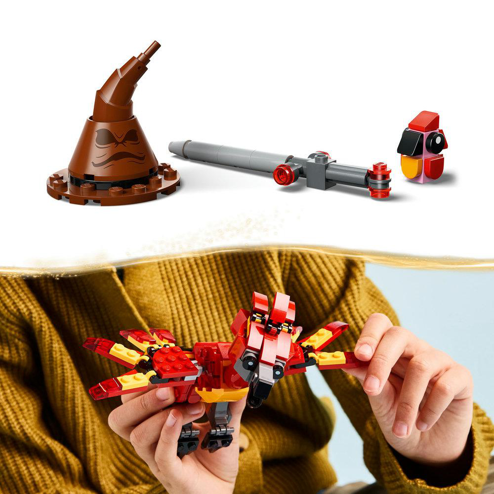 Eine Frau hält ein Lego-Vogelmodell. Der Vogel ist rot und gelb. Ein Hut und Zauberstab sind in der Nähe.