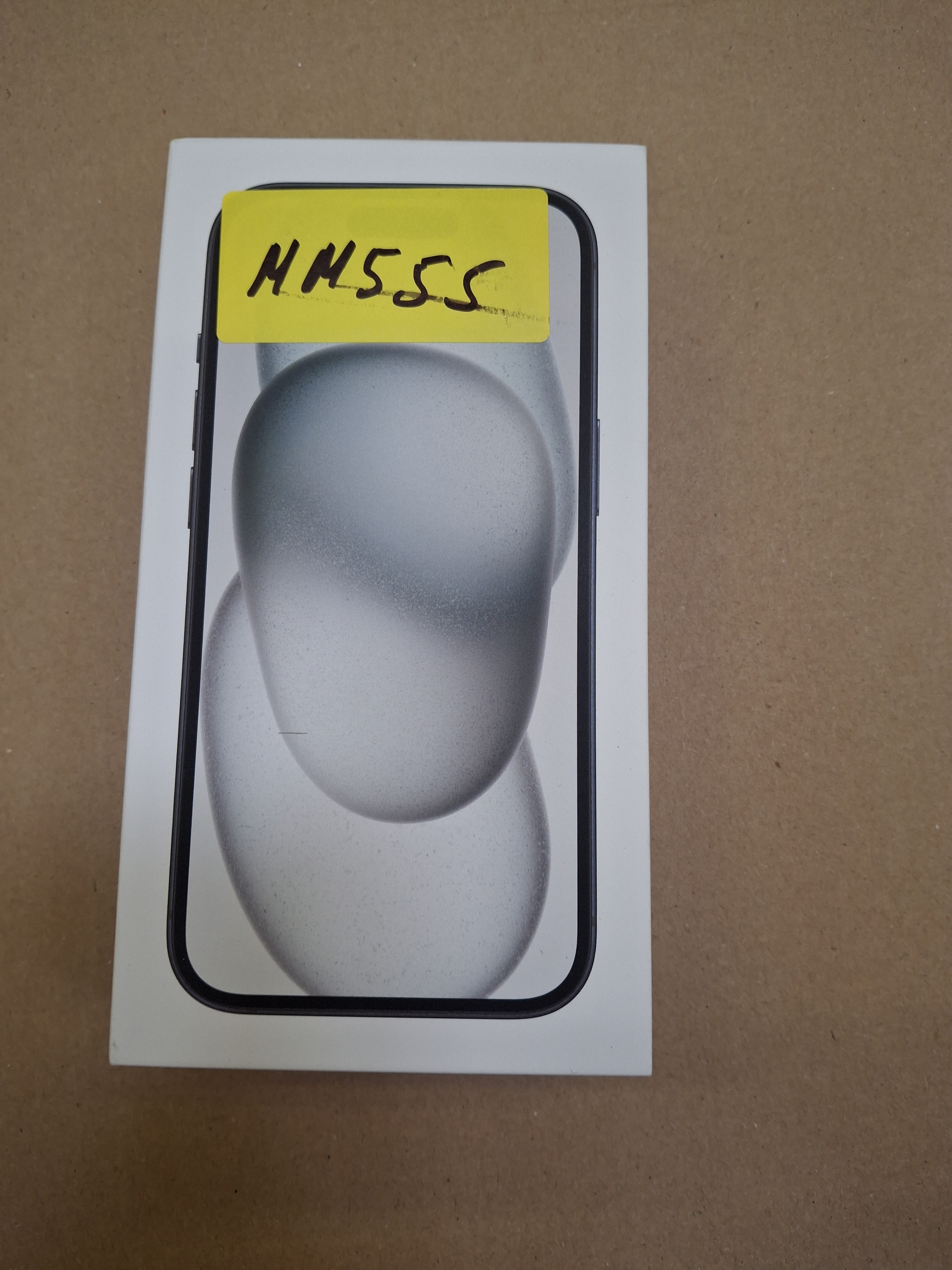 Czarny telefon w pudełku z żółtą naklejką. Telefon skierowany w górę.