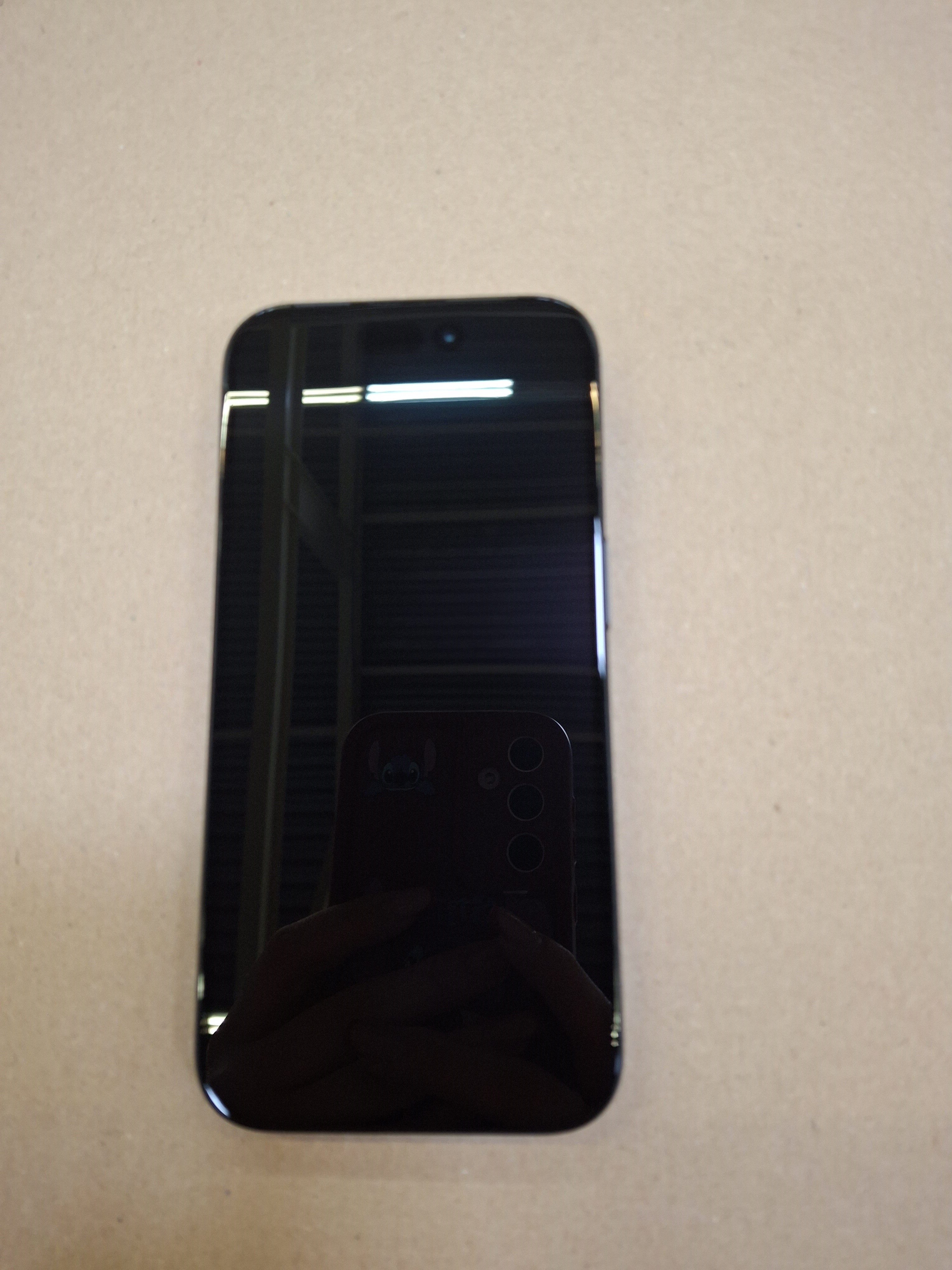 Czarny smartfon na beżowej powierzchni, odbijający moduł kamery. Telefon ma zaokrąglone rogi.