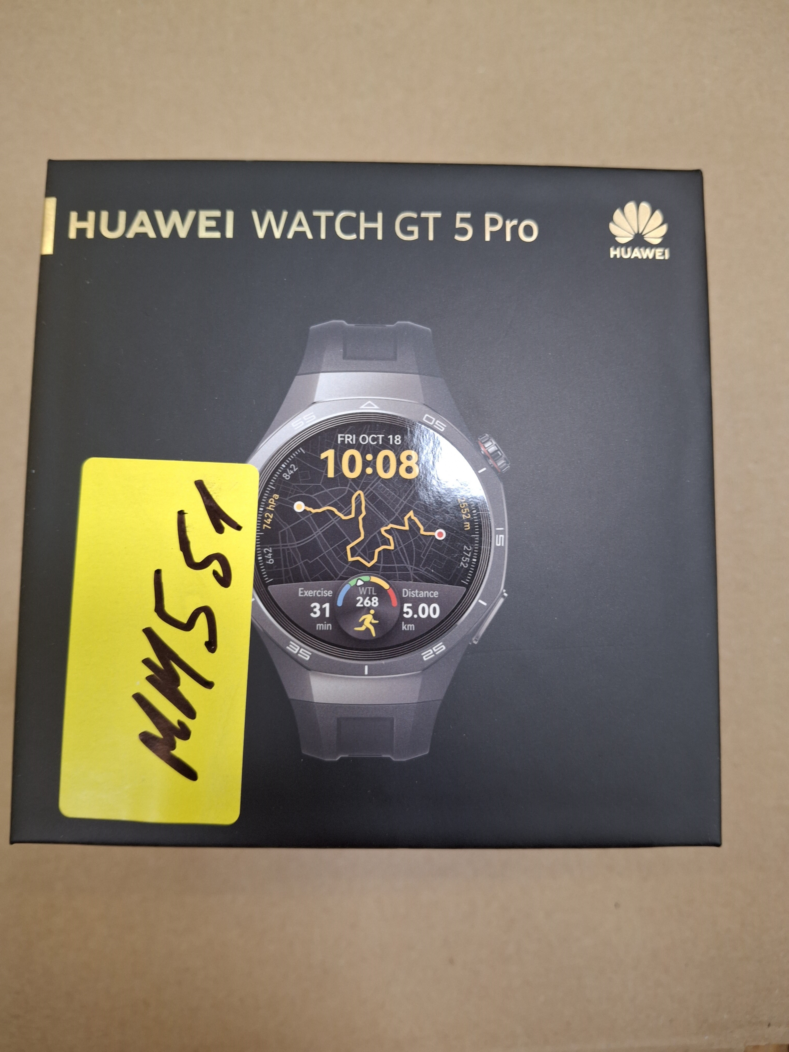 Czarne pudełko z Huawei Watch GT 5 Pro. Tarcza zegarka pokazuje czas i dane ćwiczeń. Żółta etykieta z boku.