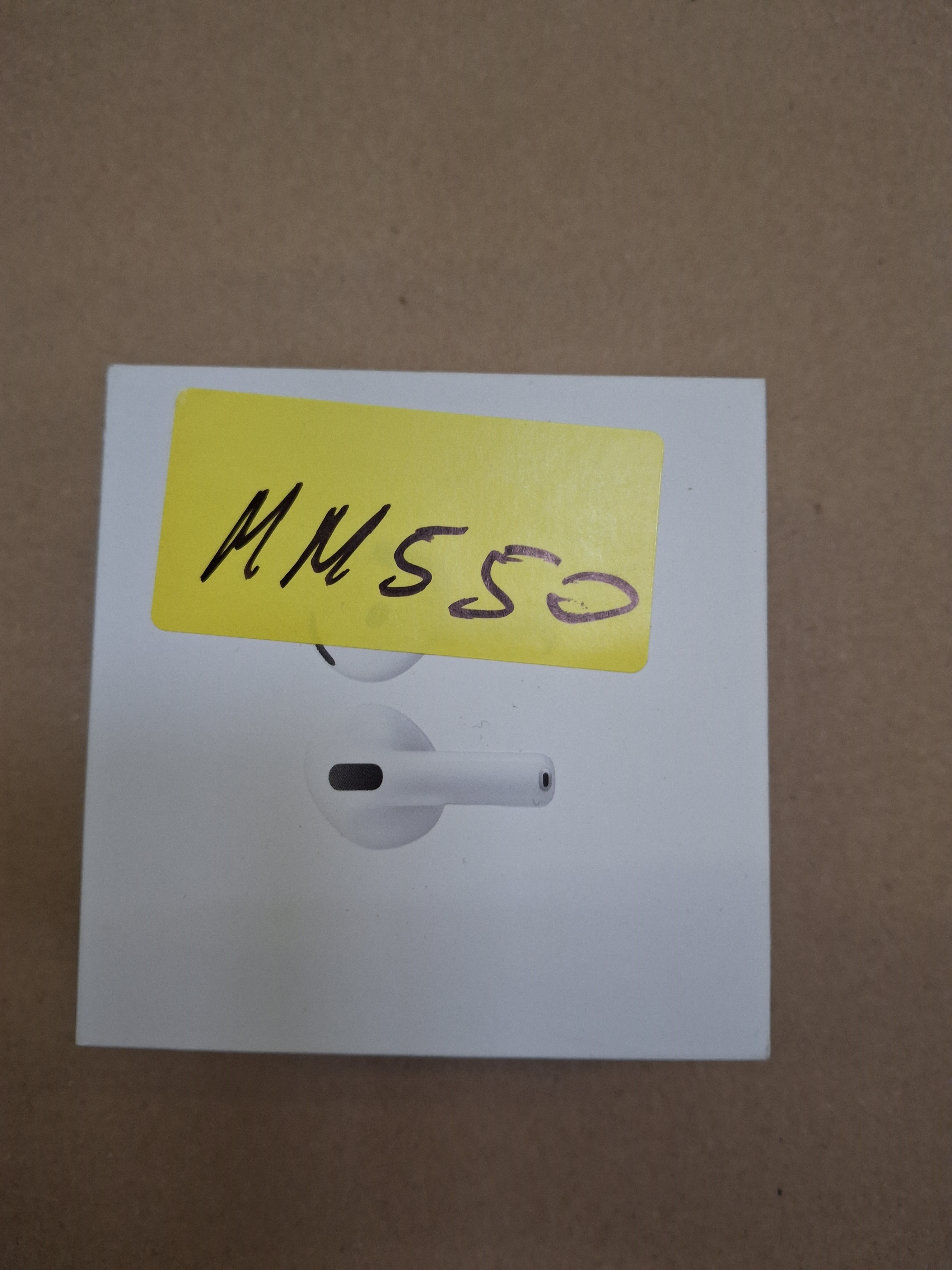 Białe pudełko z AirPods Pro. Na górze żółta etykieta. Słuchawki są białe.