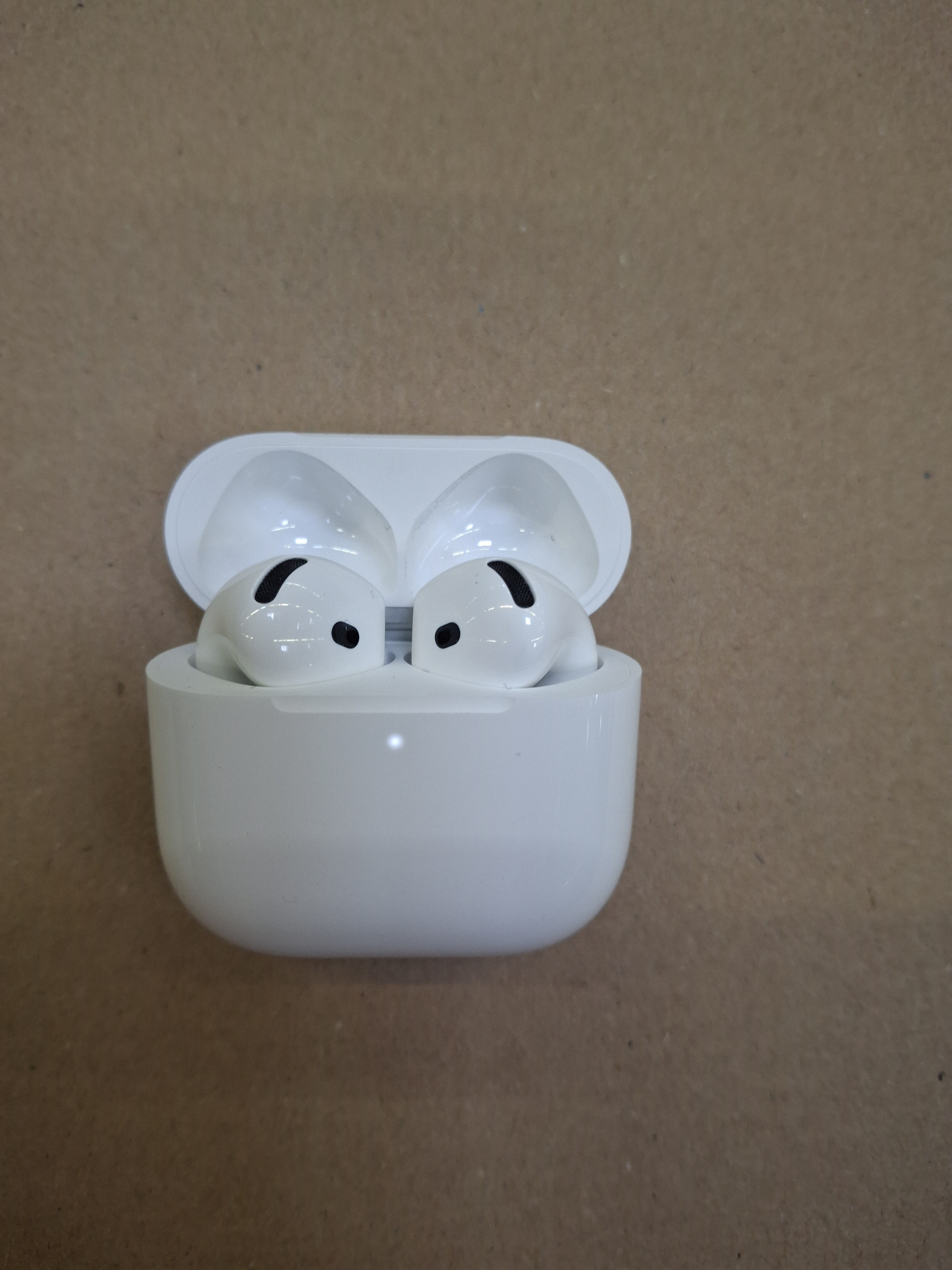 Otwarty biały futerał AirPods Pro, odsłaniający dwie białe słuchawki z czarnymi końcówkami na beżowej powierzchni.