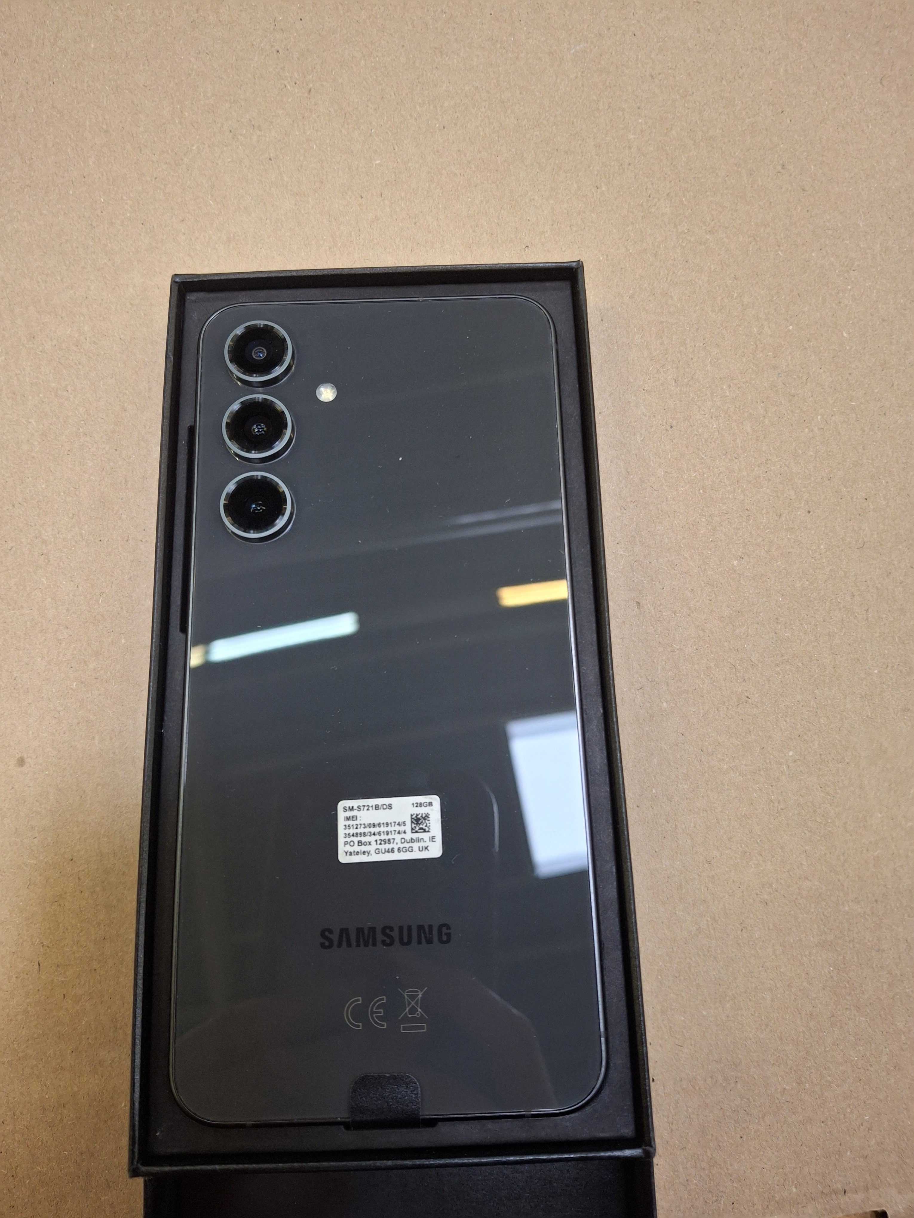 Czarny telefon na brązowej powierzchni. Trzy kamery widoczne na tylnej części. Telefon otwarty.