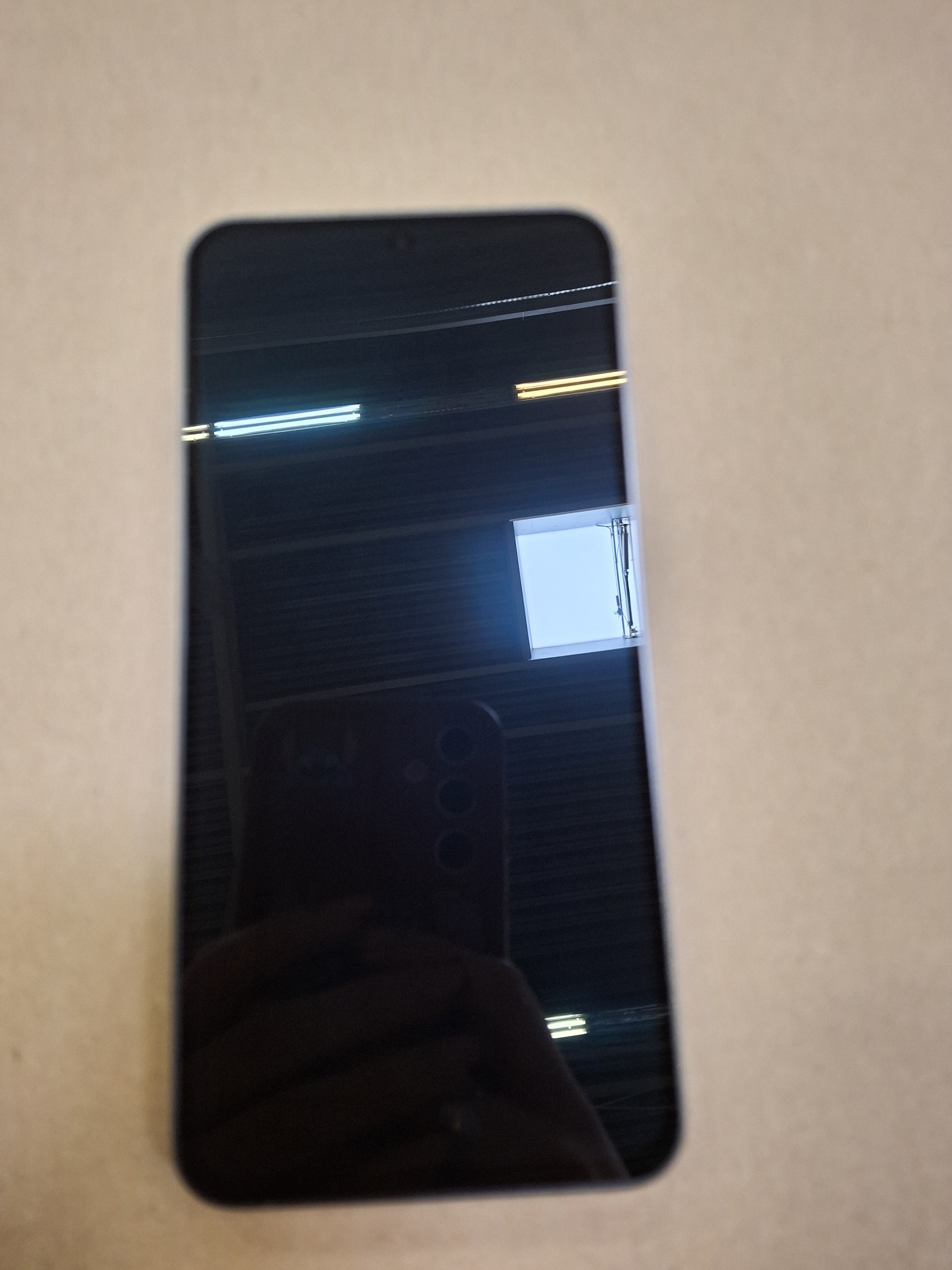 Czarny telefon z trzema kamerami, odbijający fotografa i pokój. Telefon otwarty.