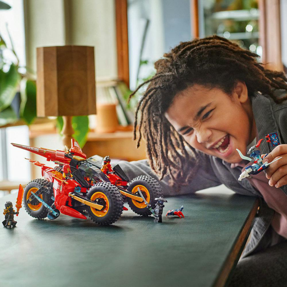 Ein Junge spielt glücklich mit einem roten LEGO-Geländewagen-Set und hält eine kleine Drachenfigur.