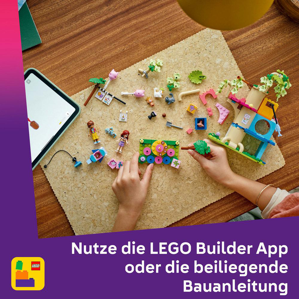 Person verwendet Lego App auf Tablet. Lego-Teile verstreut. Lego-Set mit Figuren, Baum und Gebäude.