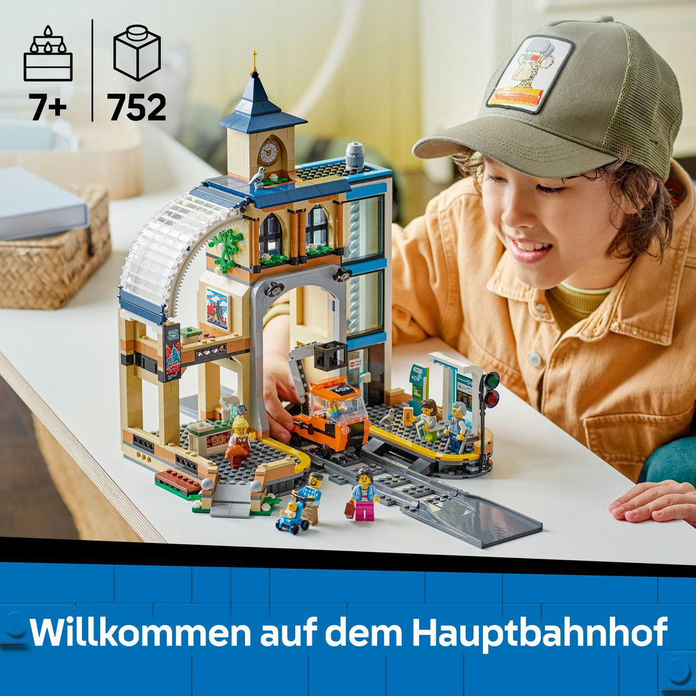 Ein Kind spielt mit einem Lego City Bahnhof-Set. Es enthält einen Zug, Figuren und ein Gebäude. Blauer Hintergrund.