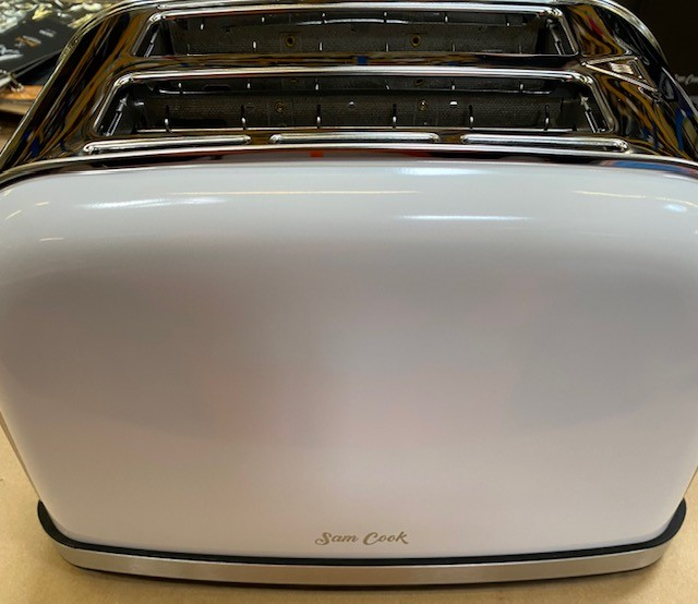 Biały toster Sam Cook z chromowanymi akcentami. Toster stoi na drewnianej powierzchni, widoczne logo.