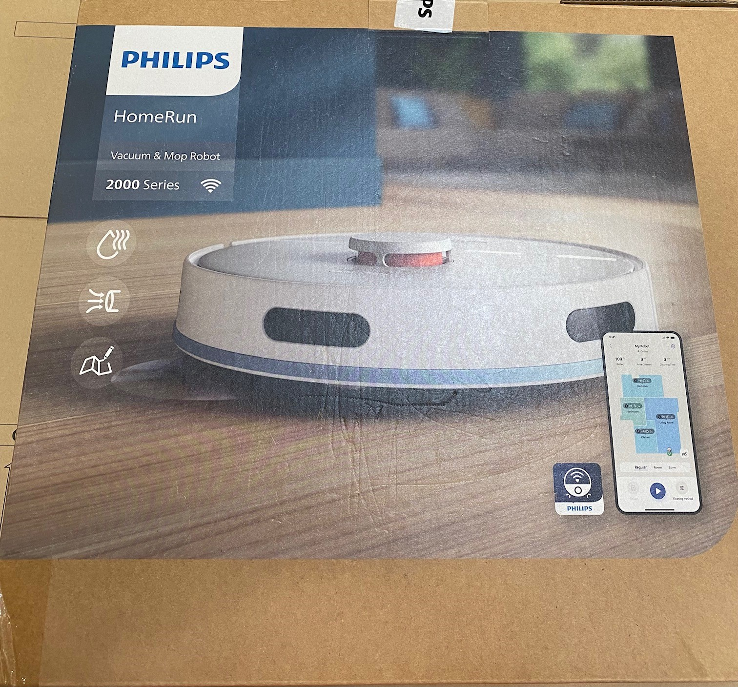 Robot odkurzający Philips HomeRun na pudełku. Telefon wyświetla aplikację. Biały robot i pudełko na drewnianej powierzchni.