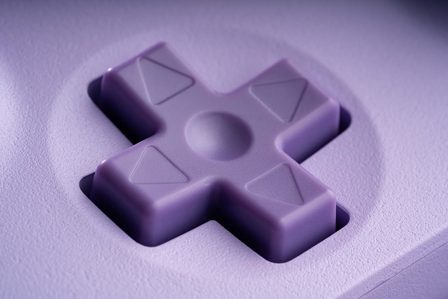 Zbliżenie krzyżaka kontrolera do gier w kolorze lawendy. W kształcie krzyża, zagłębiony w białej powierzchni.