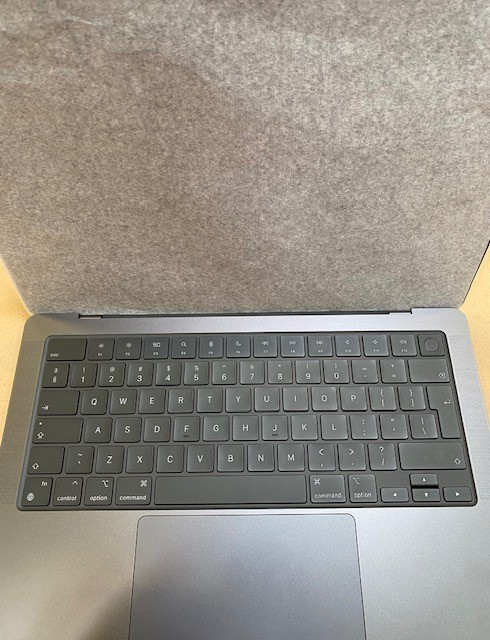 Widoczna jest klawiatura i gładzik laptopa. Klawiatura jest szara z białymi klawiszami. Szara tkanina jest na górze laptopa.