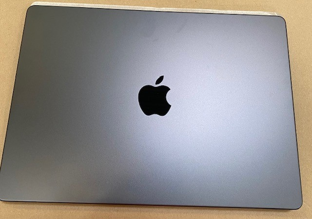 Zamknięty MacBook Pro. Górna część jest szara z czarnym logo Apple pośrodku. Spoczywa na brązowej powierzchni.