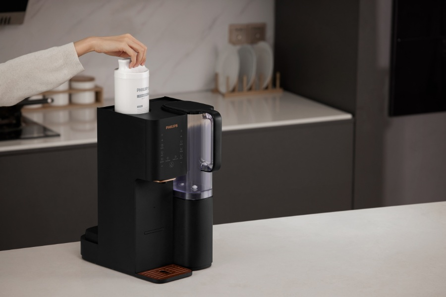 Osoba umieszcza biały filtr wody Philips w czarnym ekspresie do kawy. Tło kuchni.