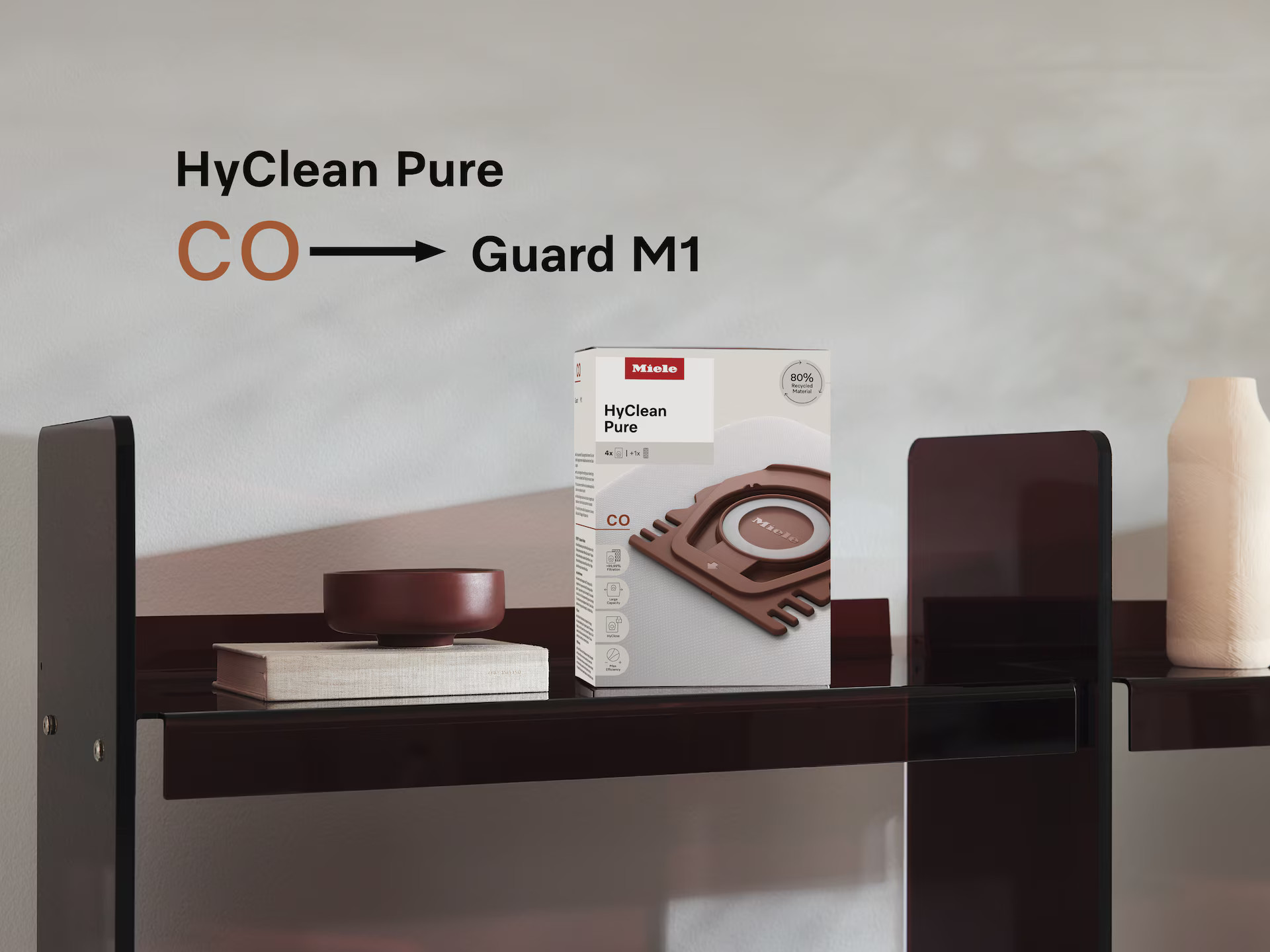 Półka z pudełkiem worka na kurz Miele, miską i wazonem. Tekst: HyClean Pure to Guard M1.