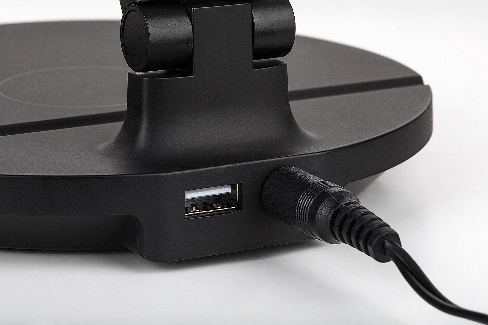 Közelkép egy fekete asztali lámpa talpáról, USB-porttal és tápkábellel.