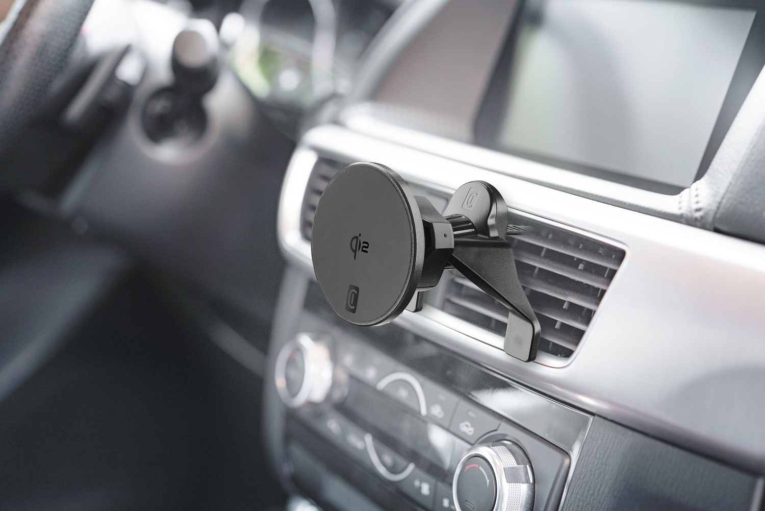 Soporte negro para teléfono de coche fijado a la ventilación. El interior del coche incluye salpicadero, controles y una pantalla.