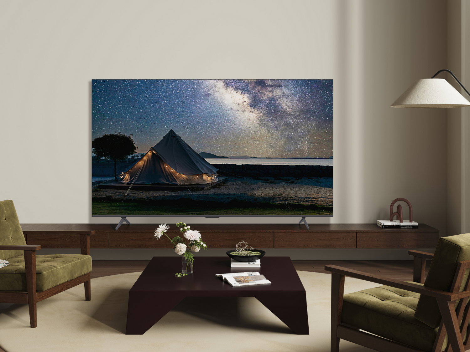 TV mostrando una escena de noche estrellada. Sobre un mueble de madera. Dos sillones verdes y una mesa.
