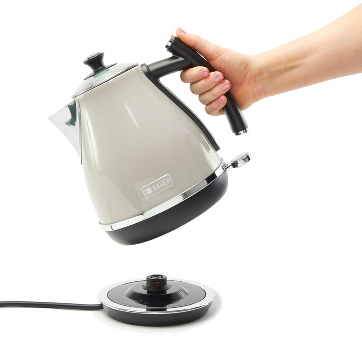 Ręka trzyma szary czajnik Haden nad podstawą. Czajnik jest częściowo przechylony.