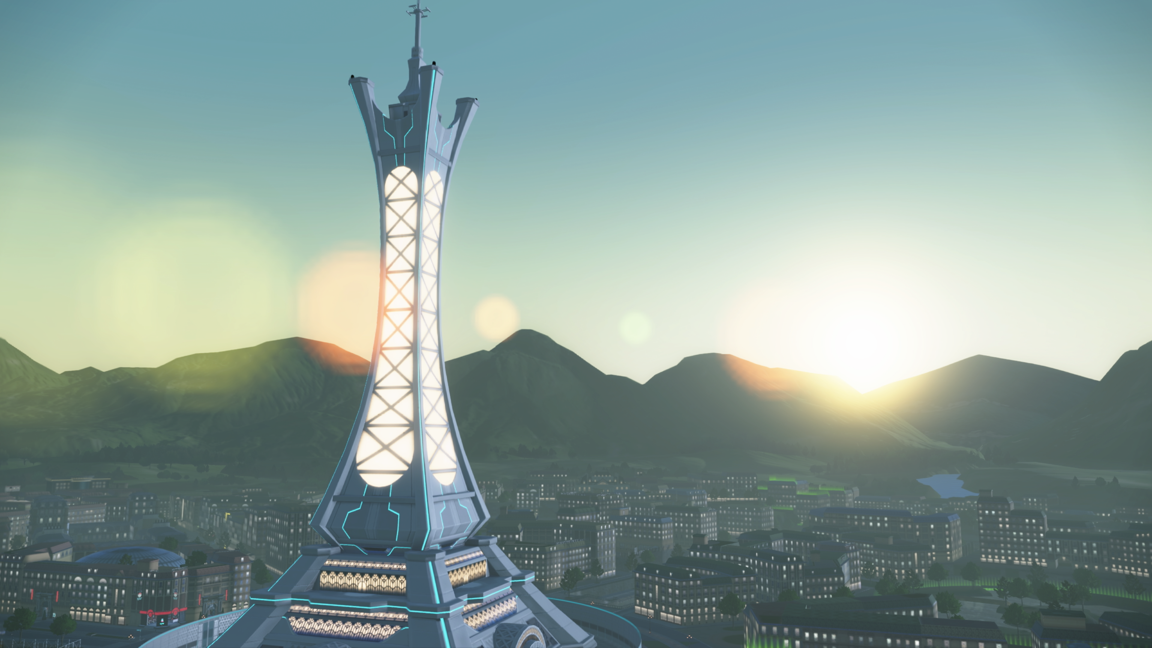 Torre con luces, ciudad y montañas al fondo al atardecer.