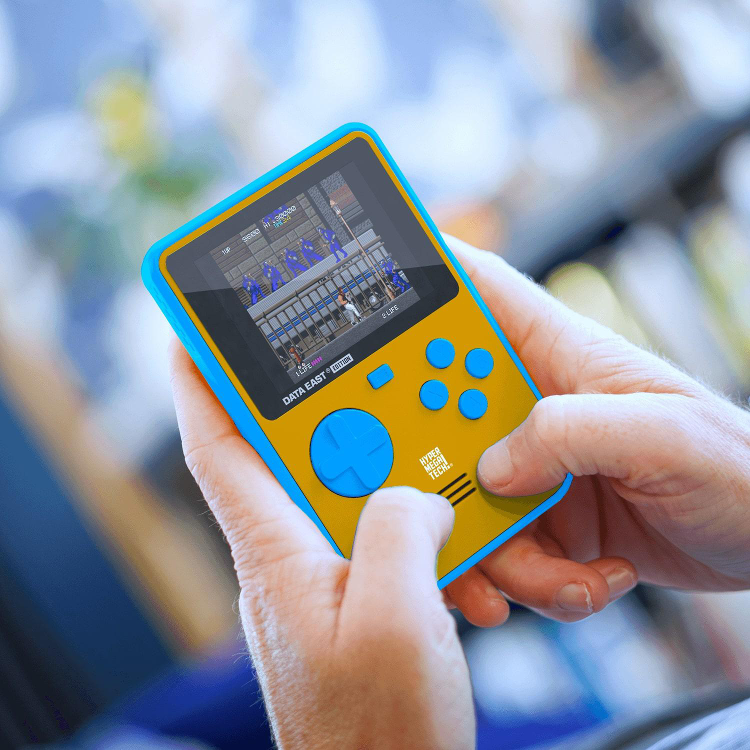 Person hält eine blau-orange Handheld-Spielkonsole. Bildschirm zeigt Retro-Spiel. Fokus auf der Konsole.