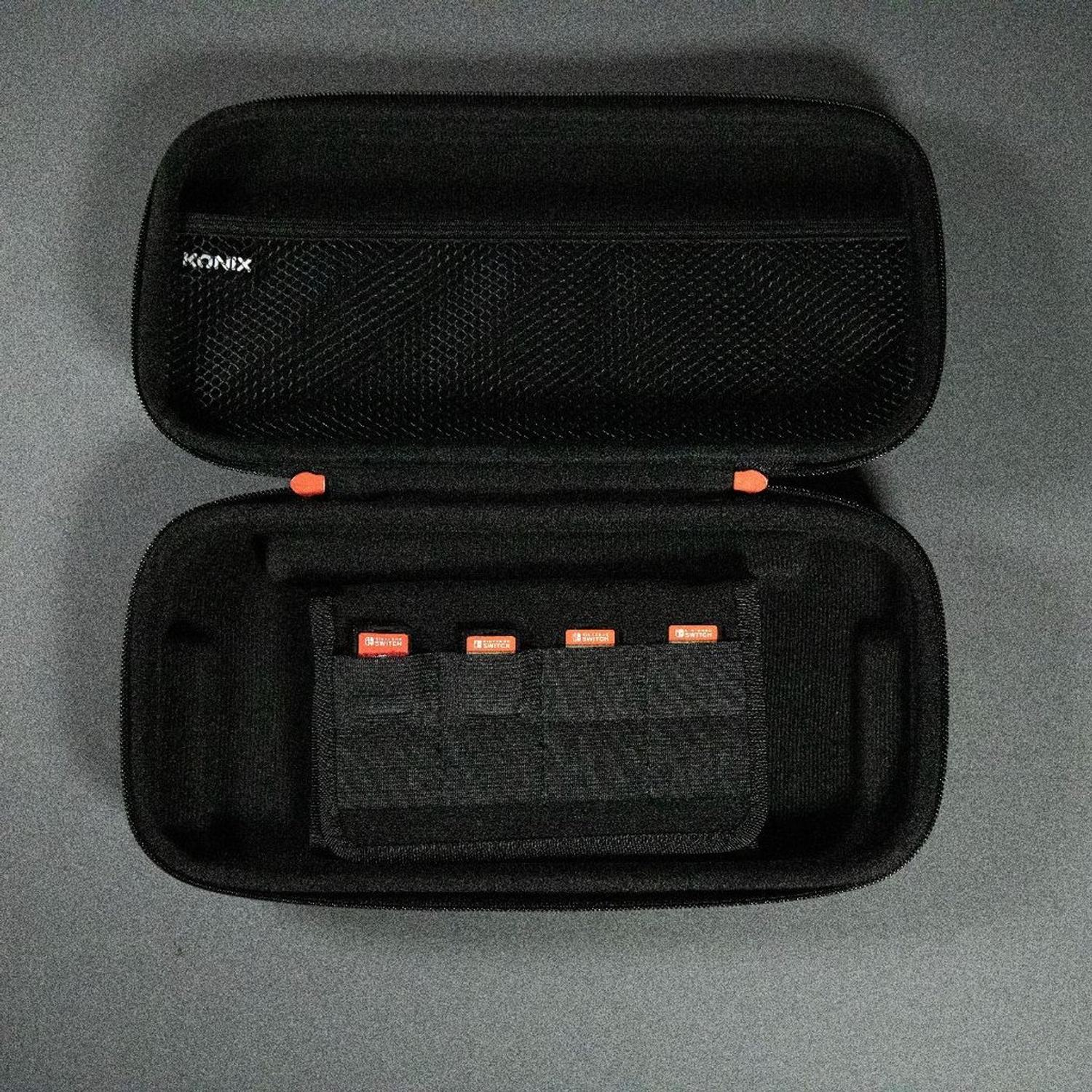 Custodia nera aperta con cartucce di gioco Switch all'interno. Logo KONIX all'interno. Superficie grigia.