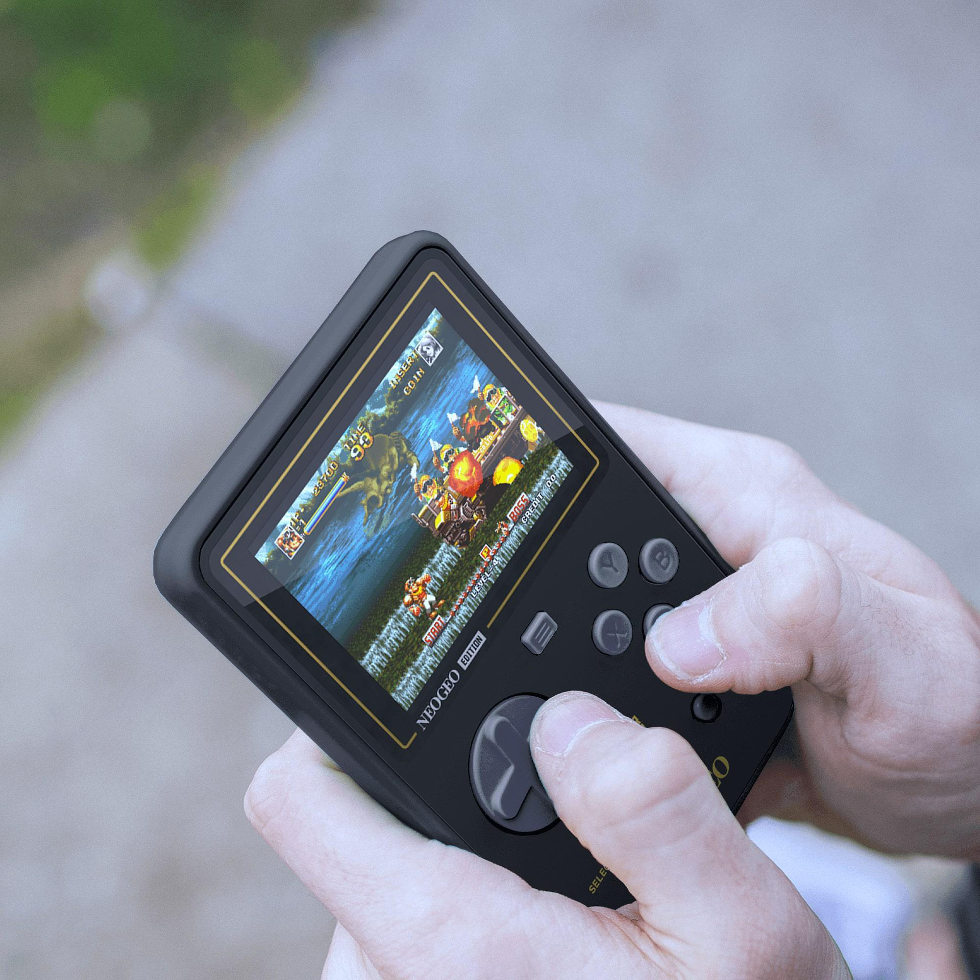 Person hält eine schwarze Handheld-Spielkonsole. Die Konsole zeigt einen Spielbildschirm. Grüner Hintergrund.