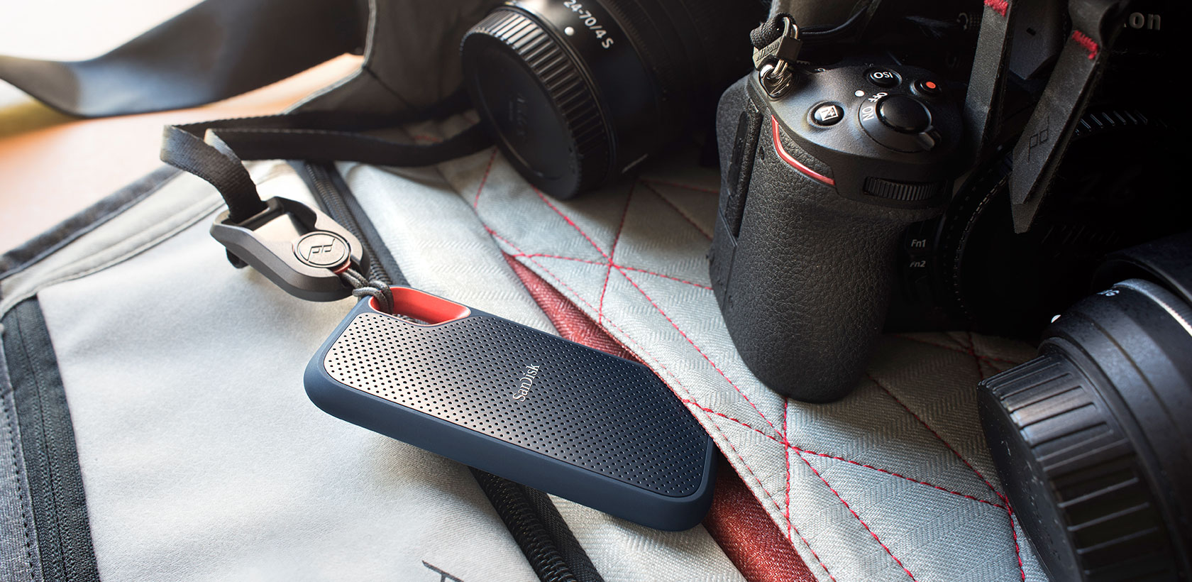 Configurazione fotocamera con disco esterno SanDisk, corpo macchina e obiettivi. Sfondo con borsa.