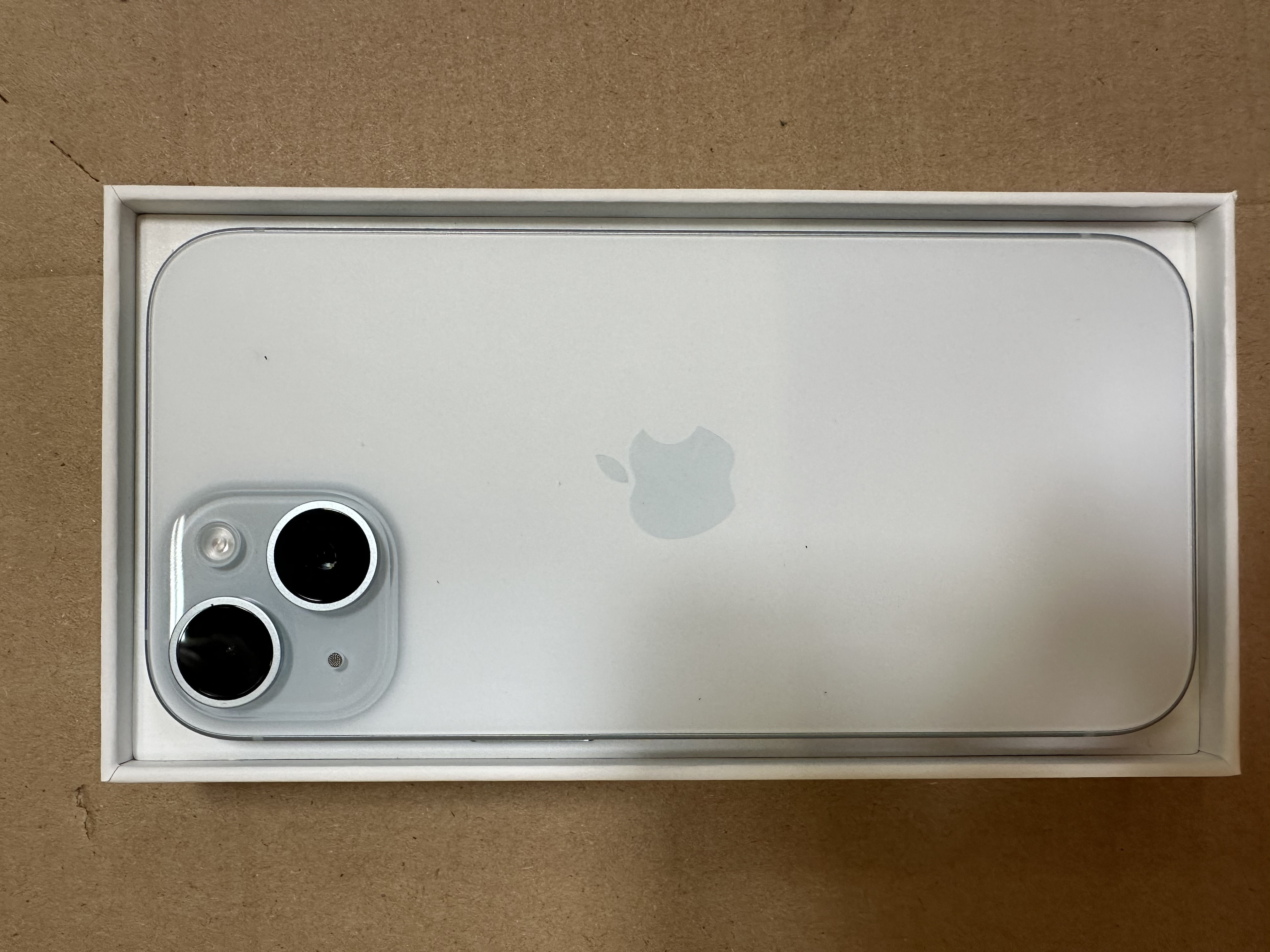 Tył białego iPhone'a w pudełku. Logo Apple i dwa obiektywy aparatu.