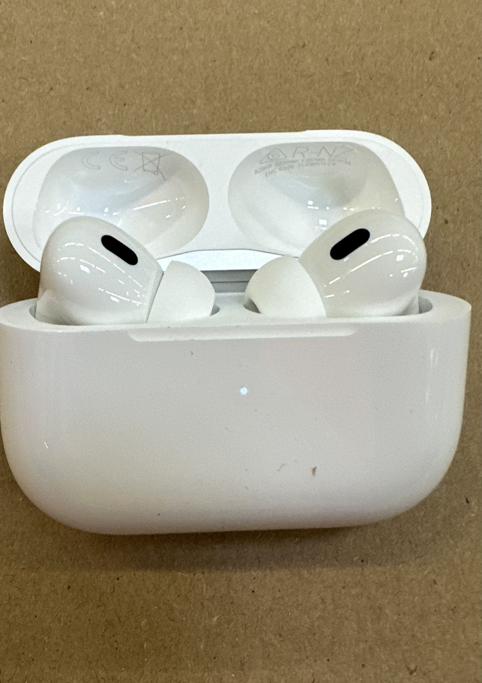Białe etui AirPods Pro otwarte z dwoma słuchawkami. Etui jest na brązowej powierzchni.