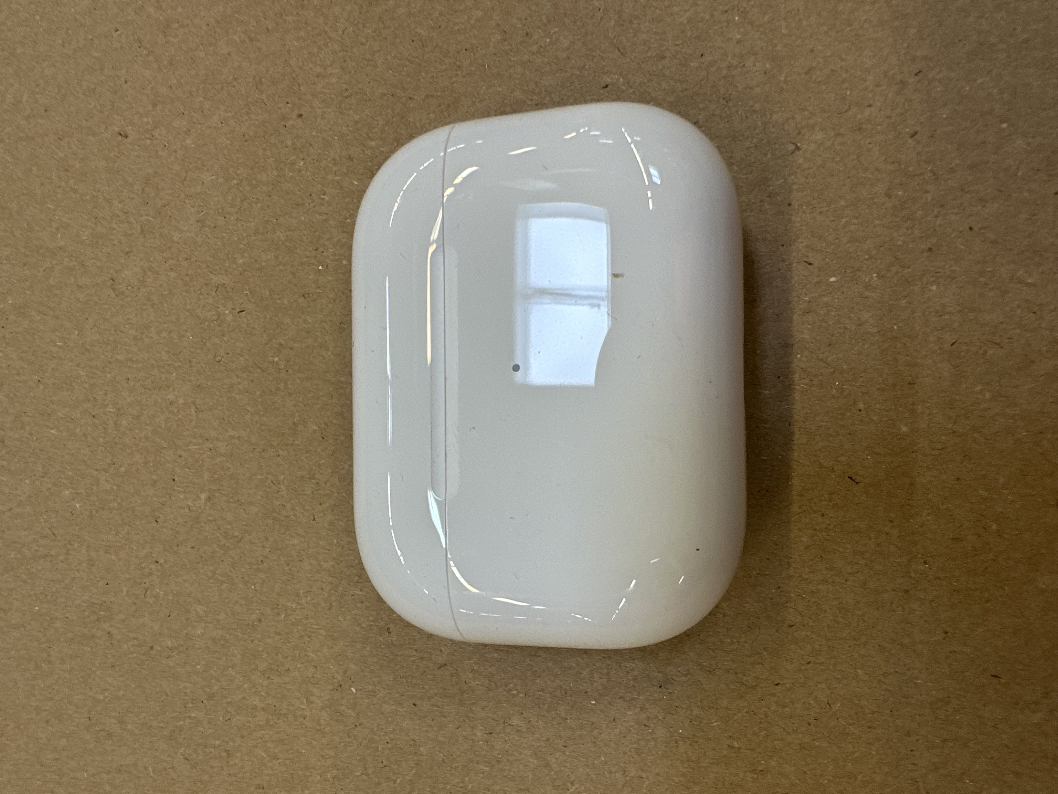 Białe etui AirPods Pro zamknięte. Na brązowej powierzchni. Etui jest błyszczące.