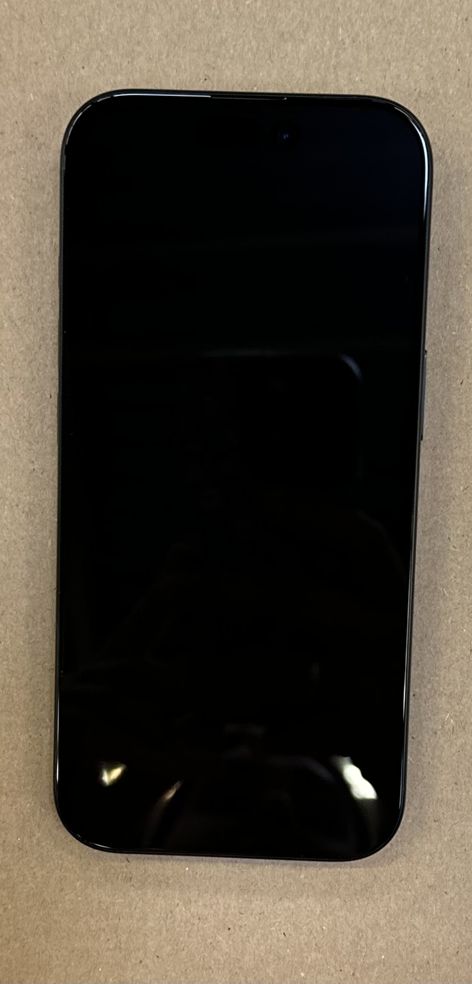 iPhone, widok z przodu. Czarny ekran, czarna ramka. Umieszczony na brązowej powierzchni.