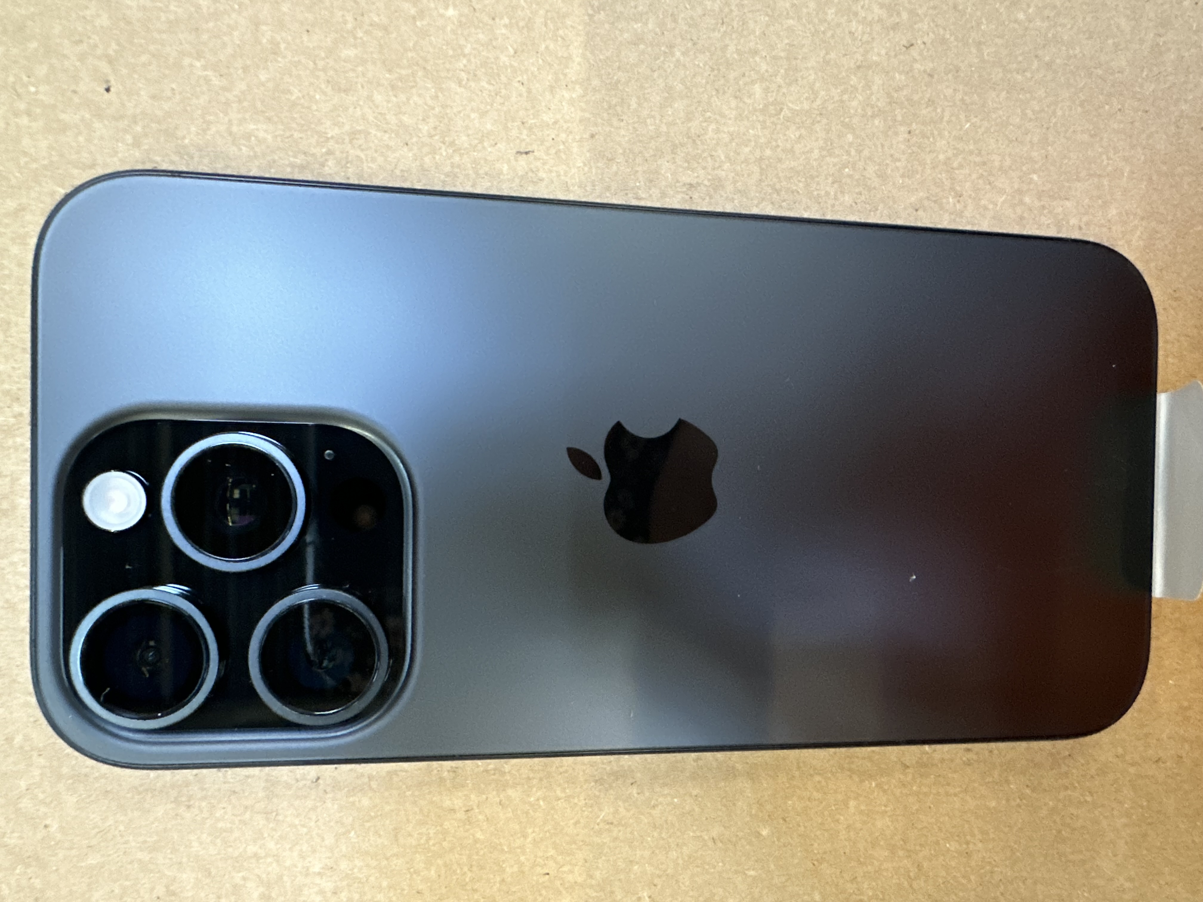 iPhone, widok z tyłu. Trzy obiektywy aparatu, logo Apple. Umieszczony na brązowej powierzchni.