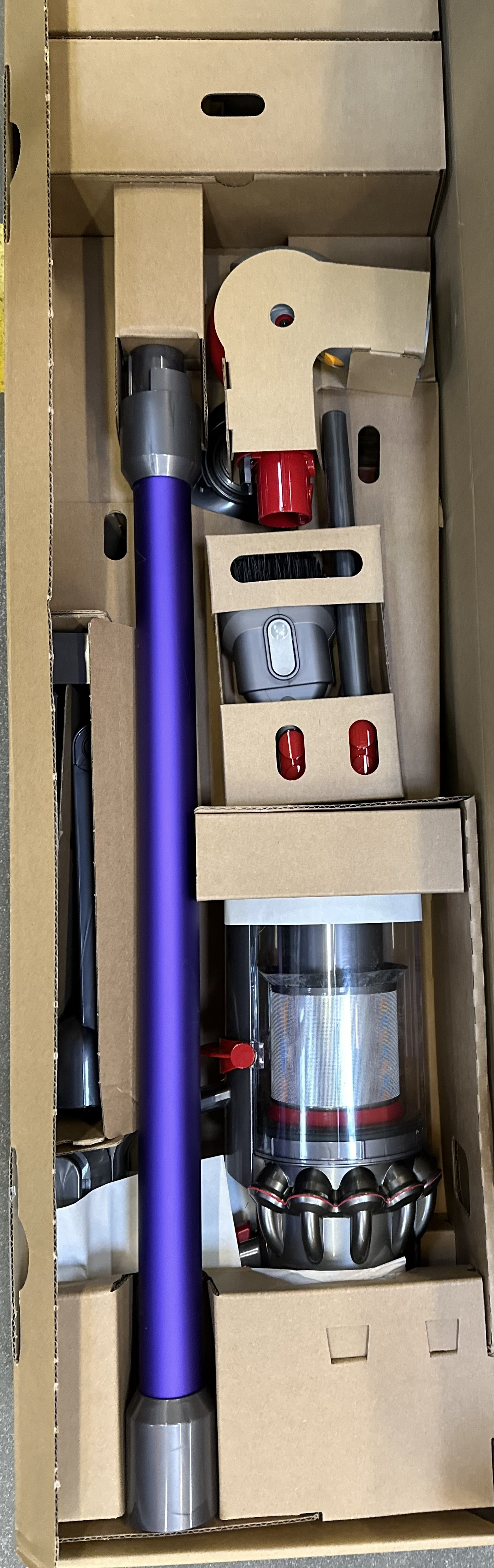 Odkurzacz w pudełku. Odkurzacz jest fioletowo-czarny, z różnymi załącznikami.