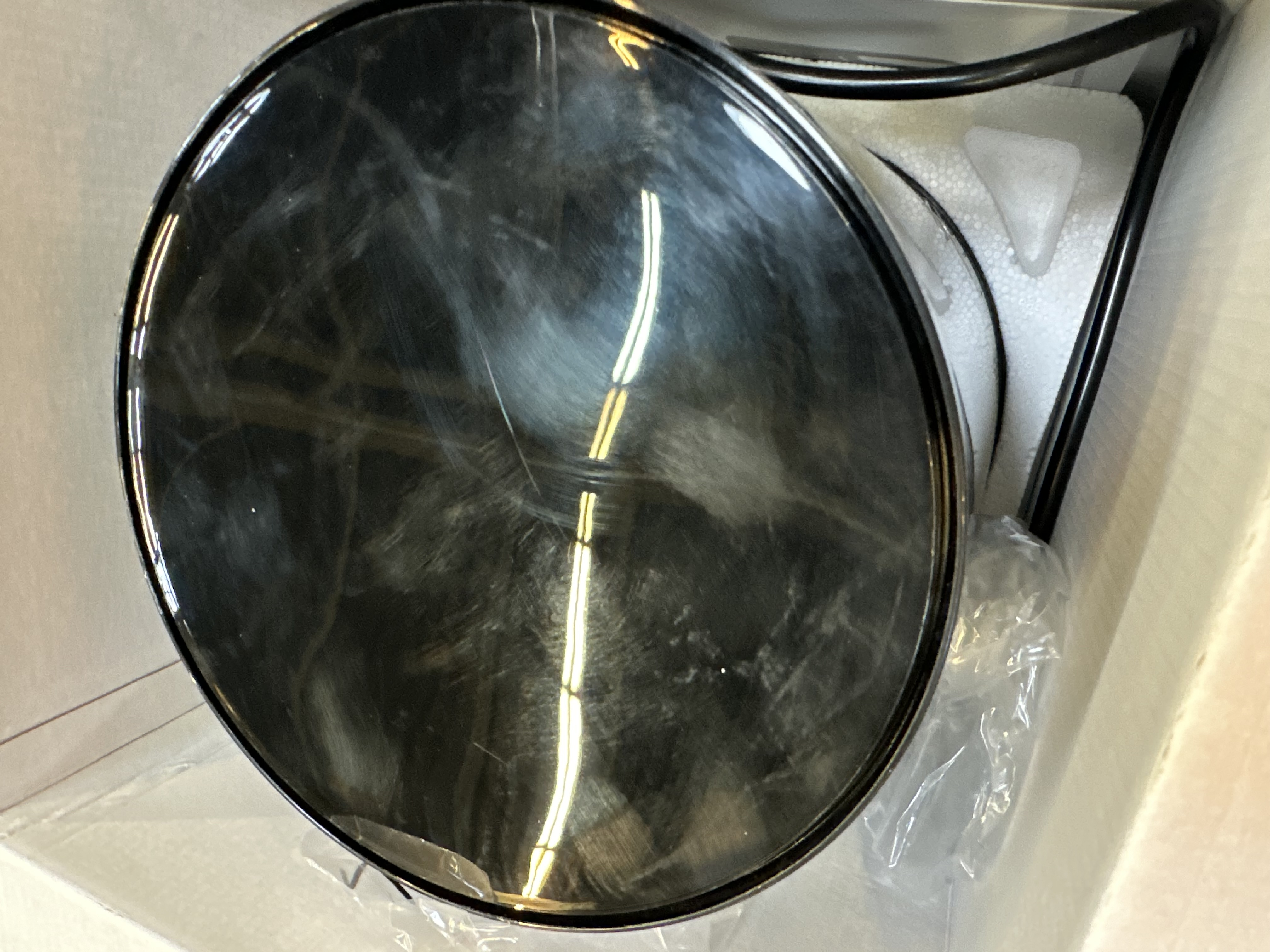 Czarny, błyszczący, okrągły przedmiot w pudełku. Obiekt odbija światło i ma ciemną krawędź.