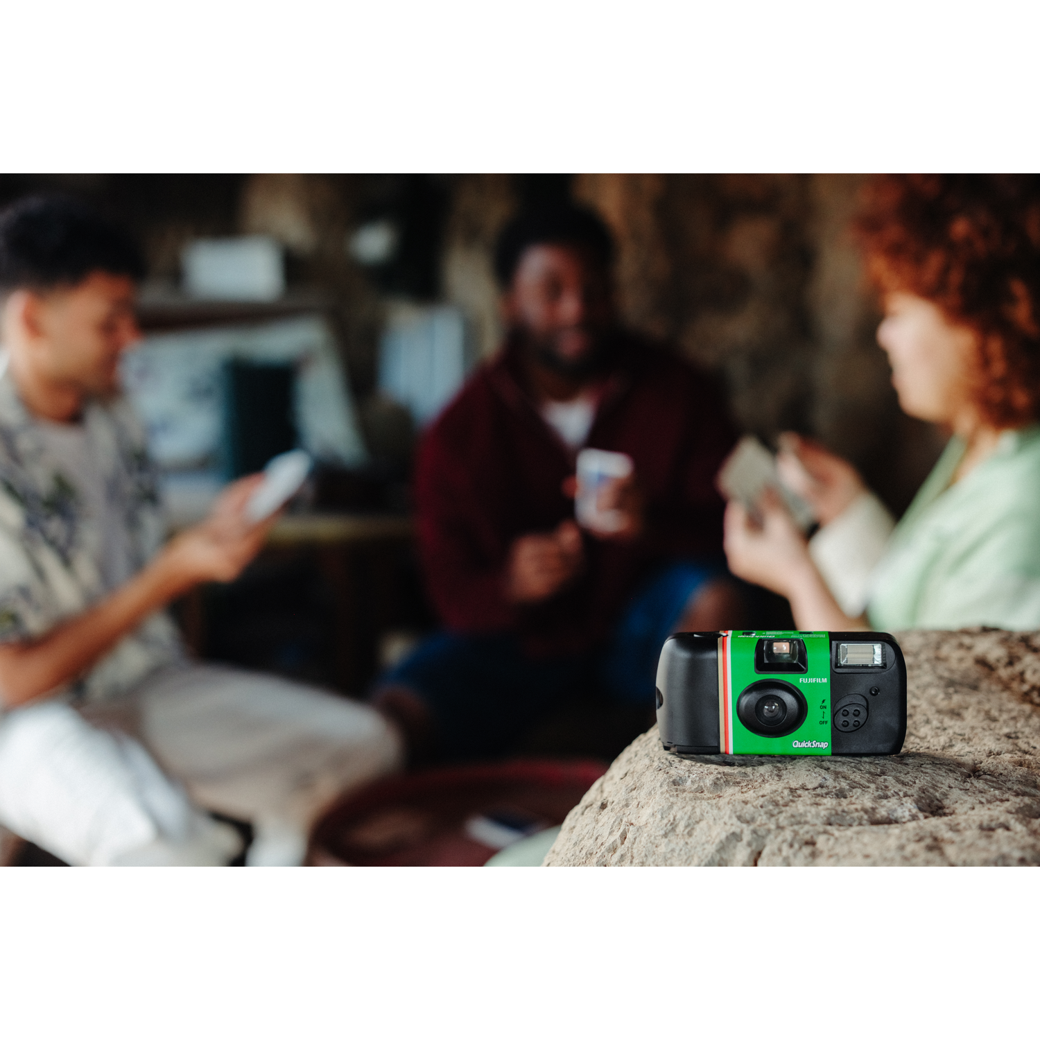 Appareil photo QuickSnap sur un rocher avec trois personnes en arrière-plan flou.