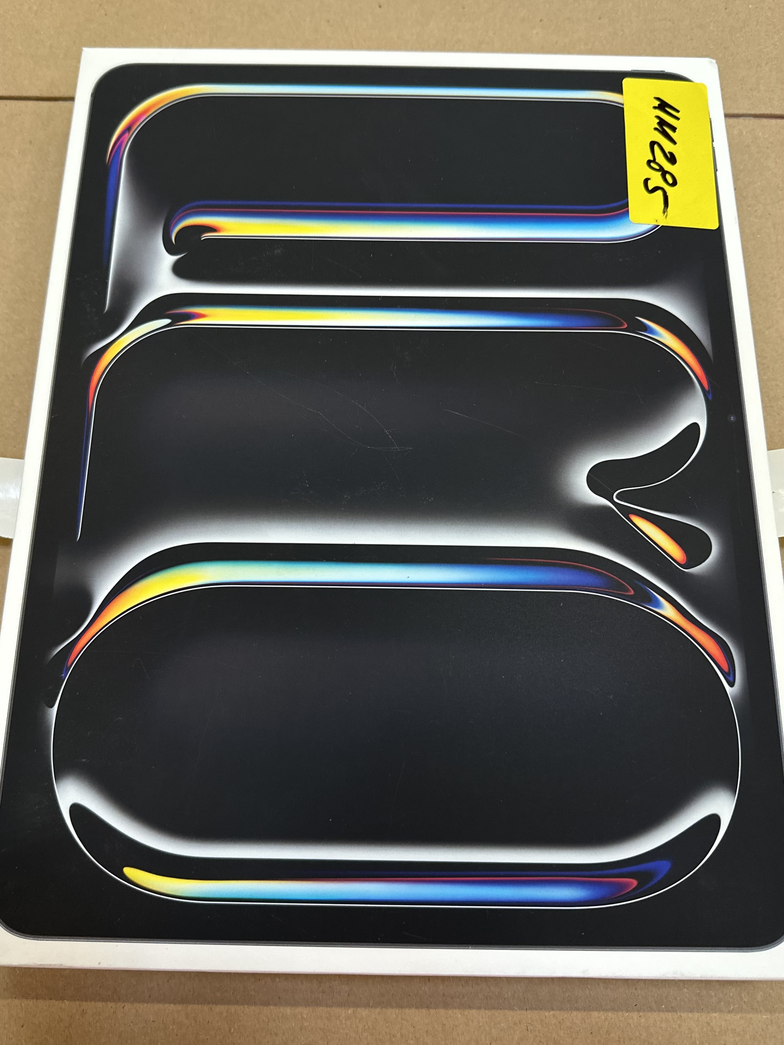 Czarne i kolorowe pudełko o zakrzywionym designie. Żółta naklejka z napisem.