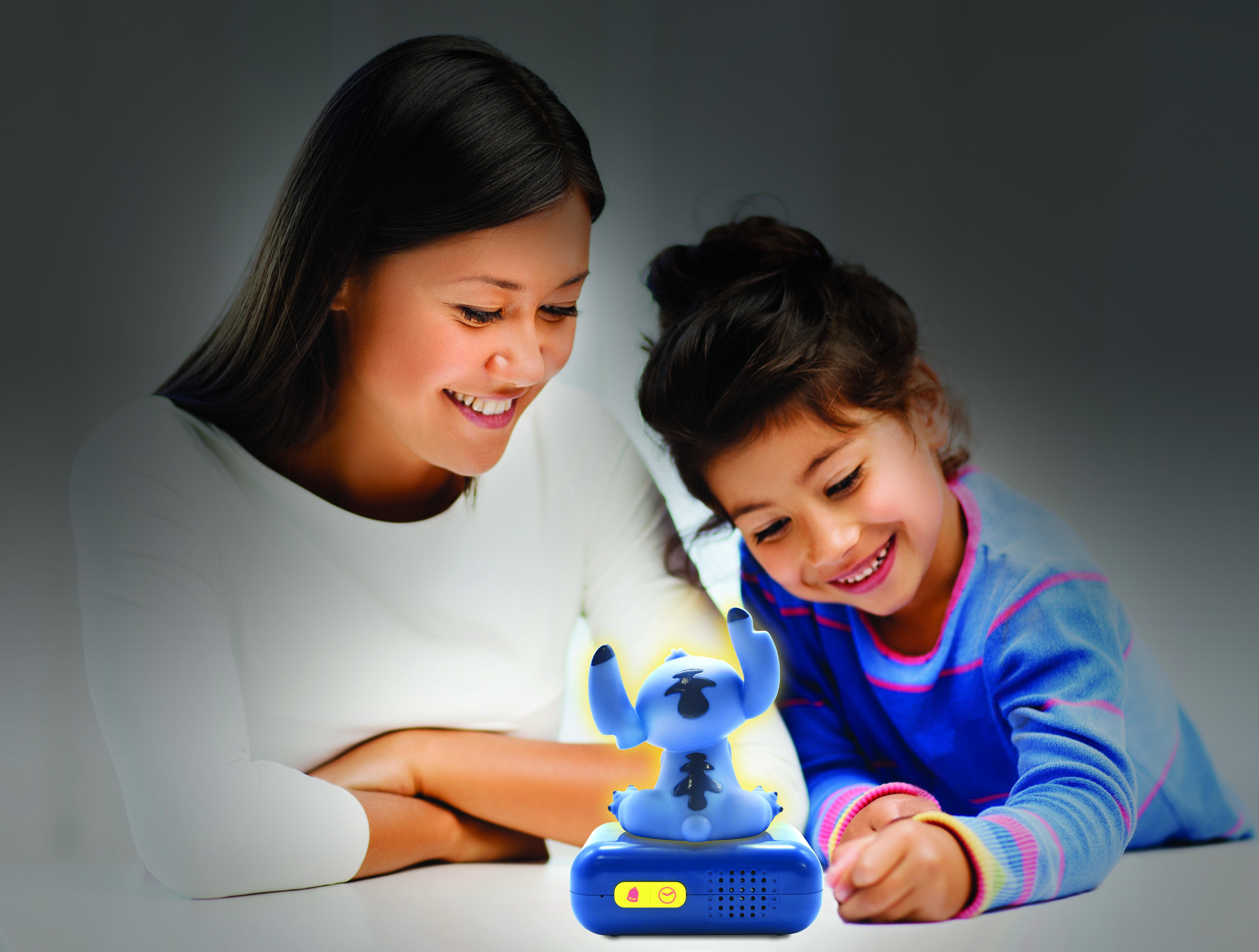 Eine Frau und ein Mädchen schauen sich eine Stitch-Lampe an. Die Lampe steht auf einem blauen Sockel und hat einen gelben Knopf.