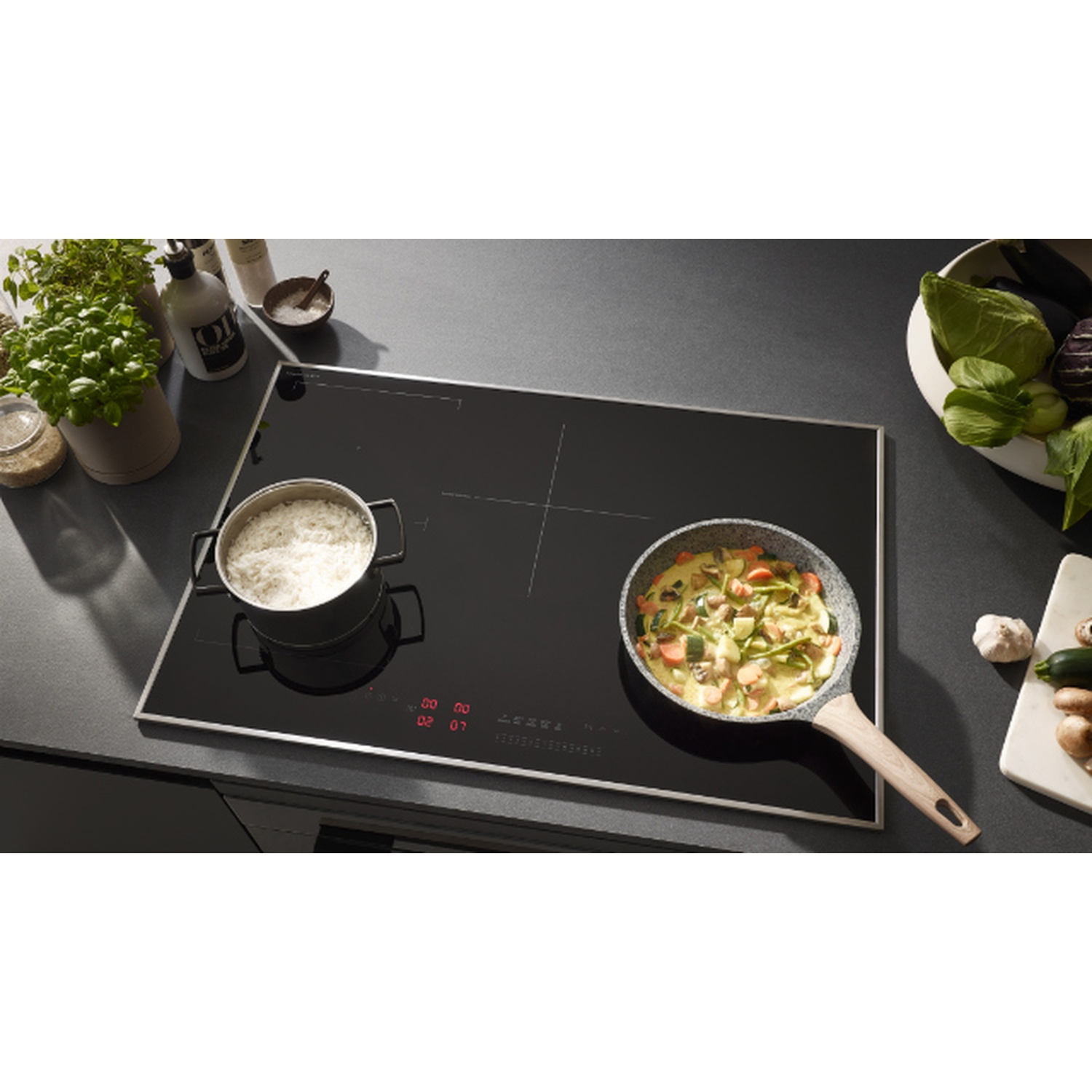 Piano cottura a induzione nero con pentola e padella. Verdure e ingredienti sono visibili.