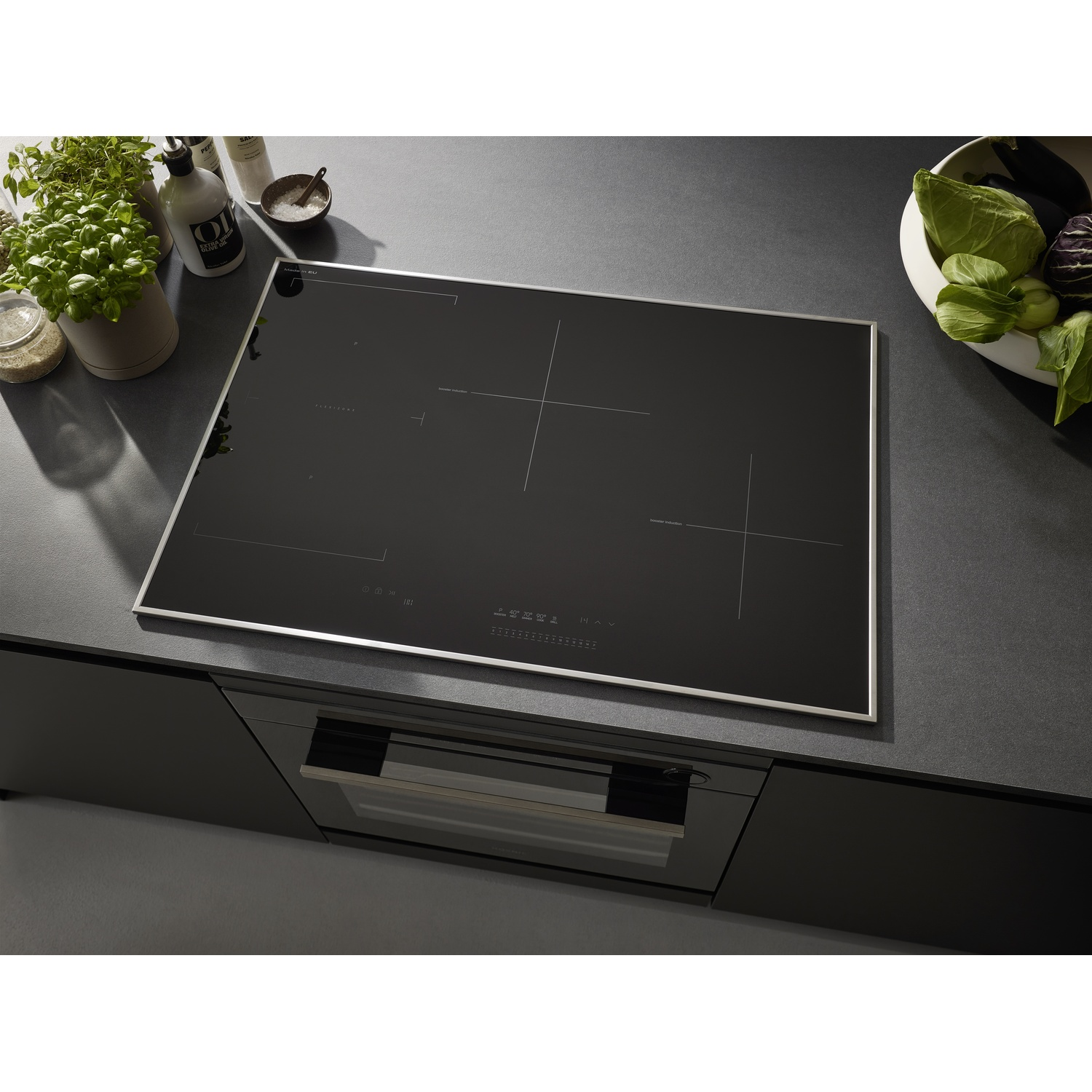 Un piano cottura a induzione nero installato in una cucina con cornice in acciaio inox. Sono visibili piante e altri oggetti.