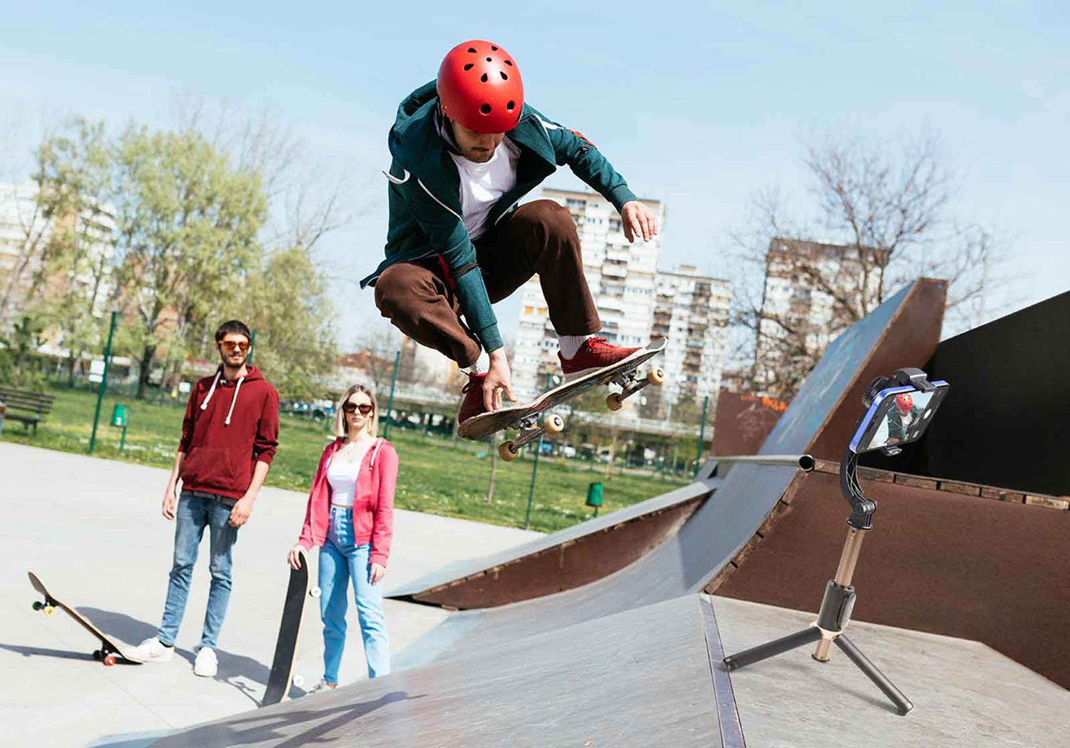 Ein Skateboarder in der Luft, mit zwei Zuschauern und einem telefonierenden Stativ.