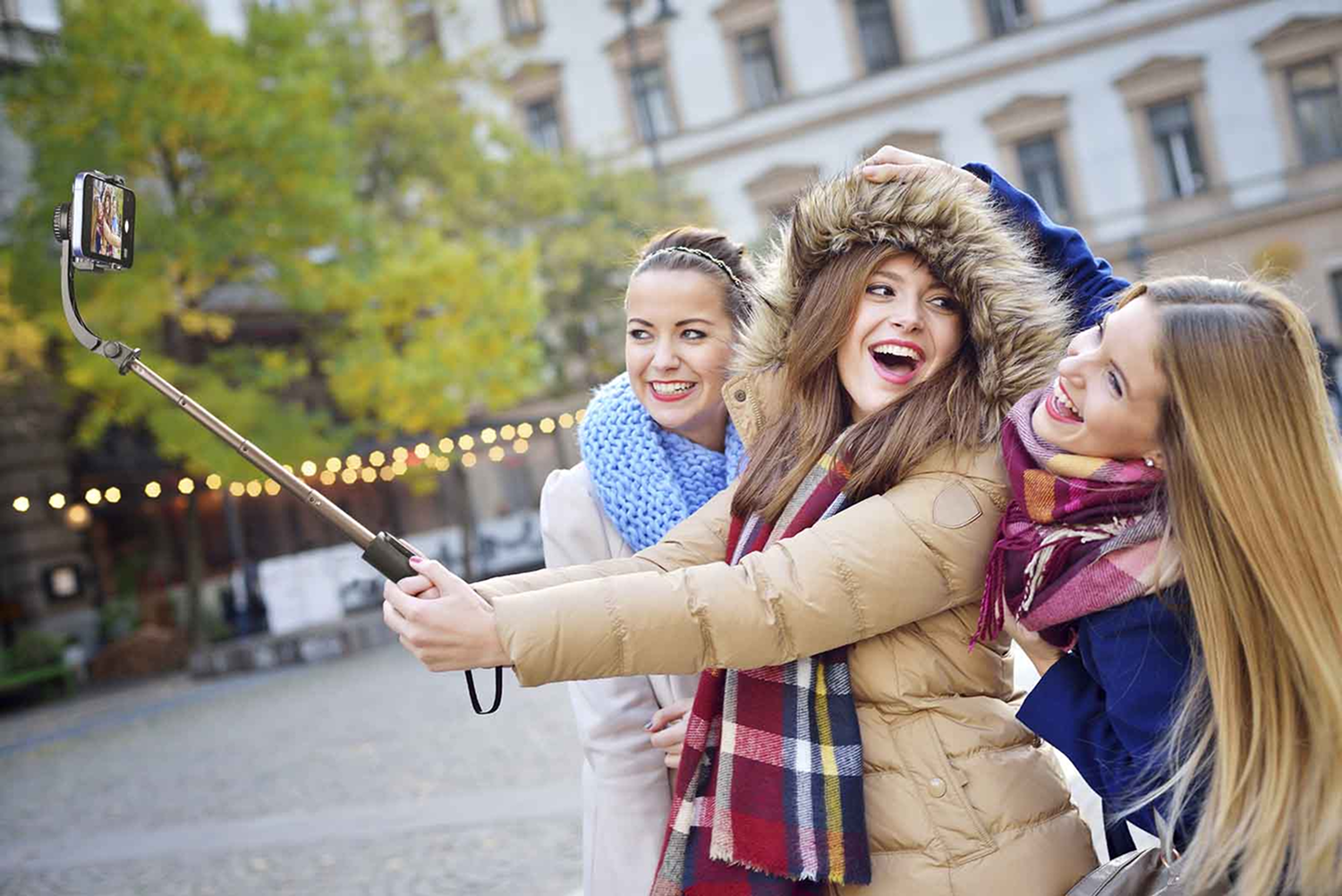 Drei Frauen machen ein Selfie mit einem Selfie-Stick, lächeln und lachen, im Winter.