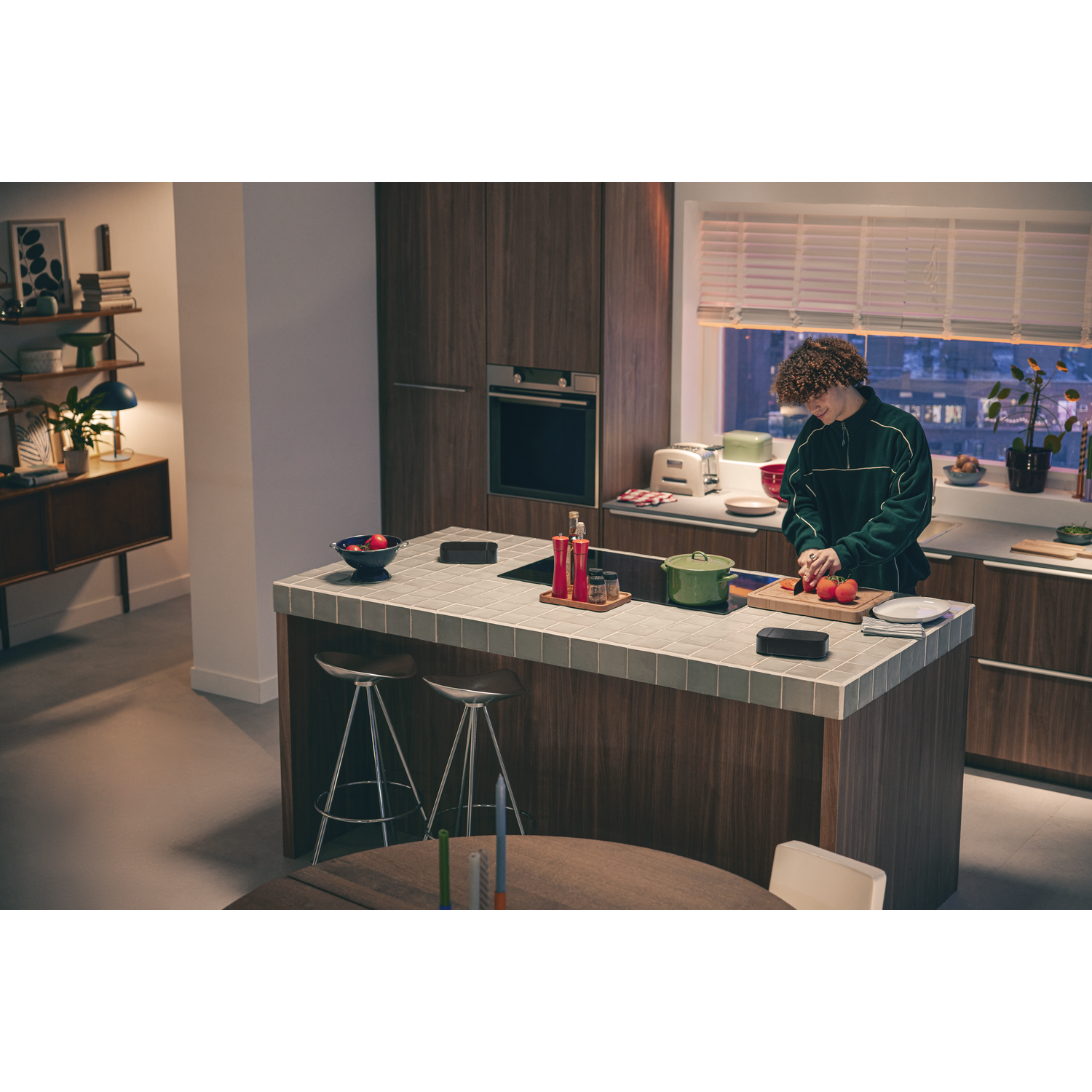Une personne coupe des légumes dans une cuisine moderne avec une barre de son JBL sur le comptoir.