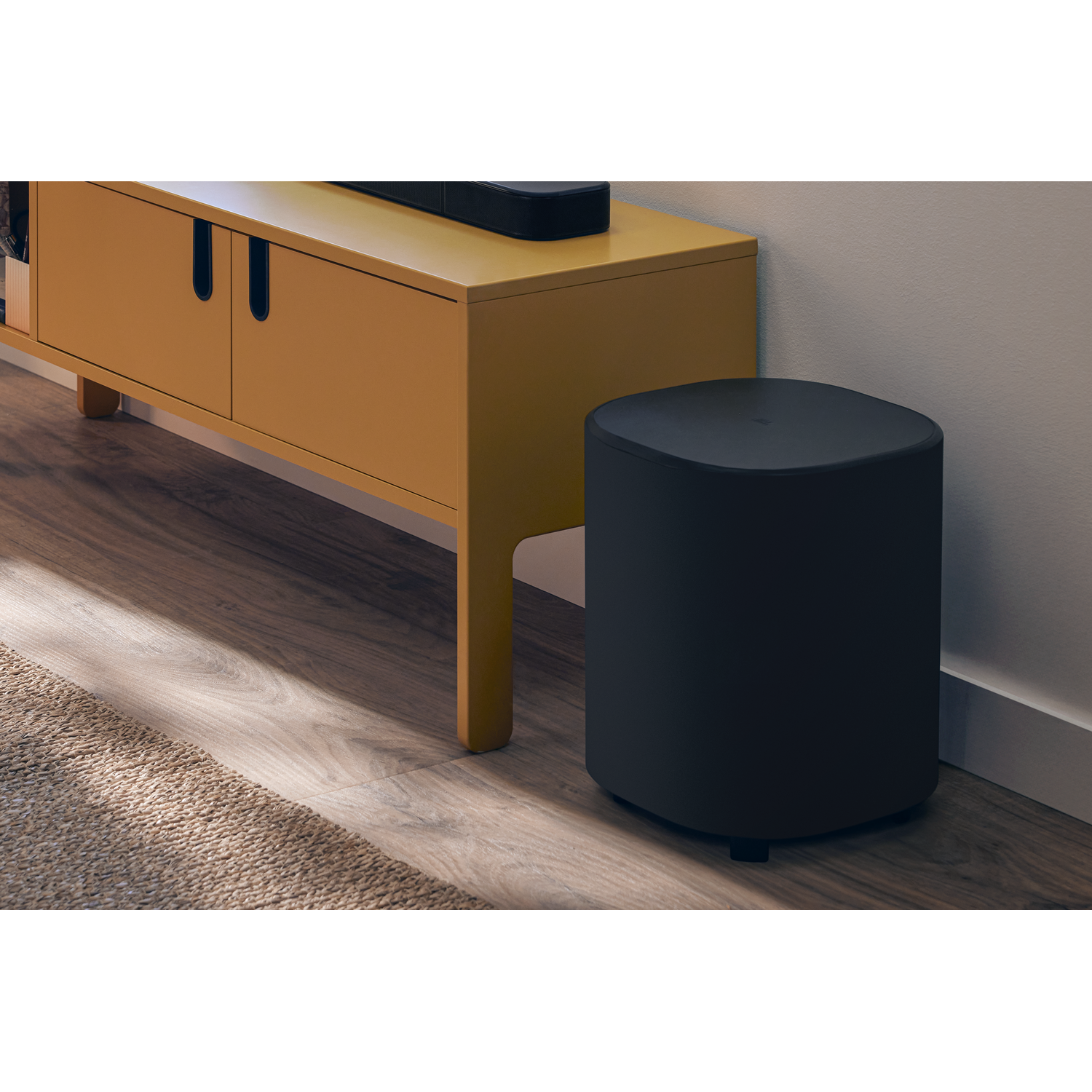 Un caisson de basses JBL et un meuble jaune. Le caisson est noir et sur parquet.